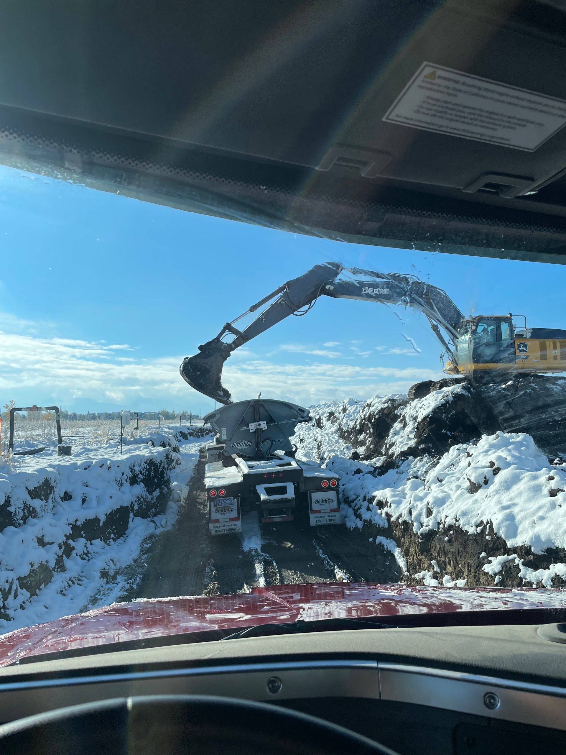 A truck is driving down a snowy road next to a large excavator.