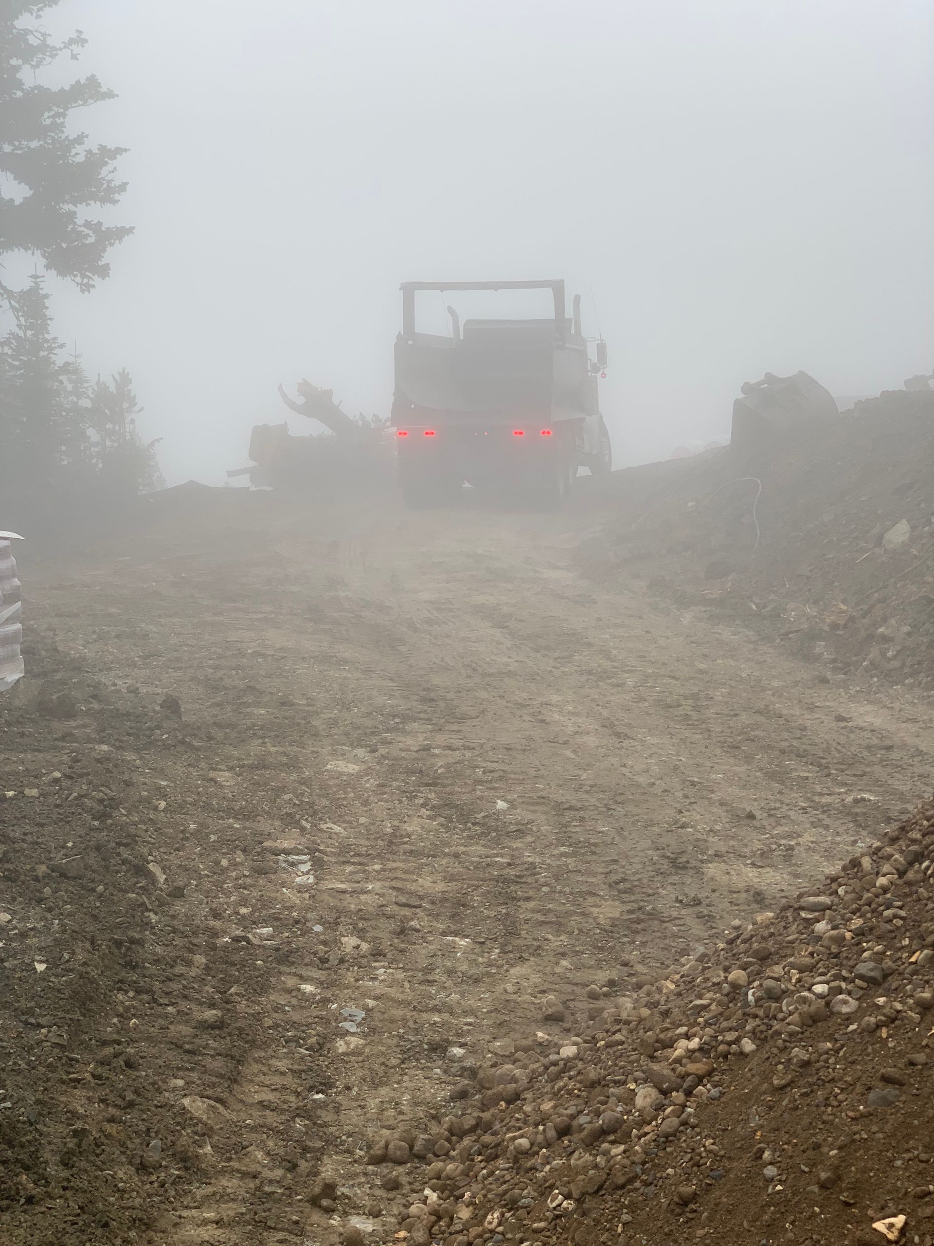 A truck is driving down a dirt road in the fog.