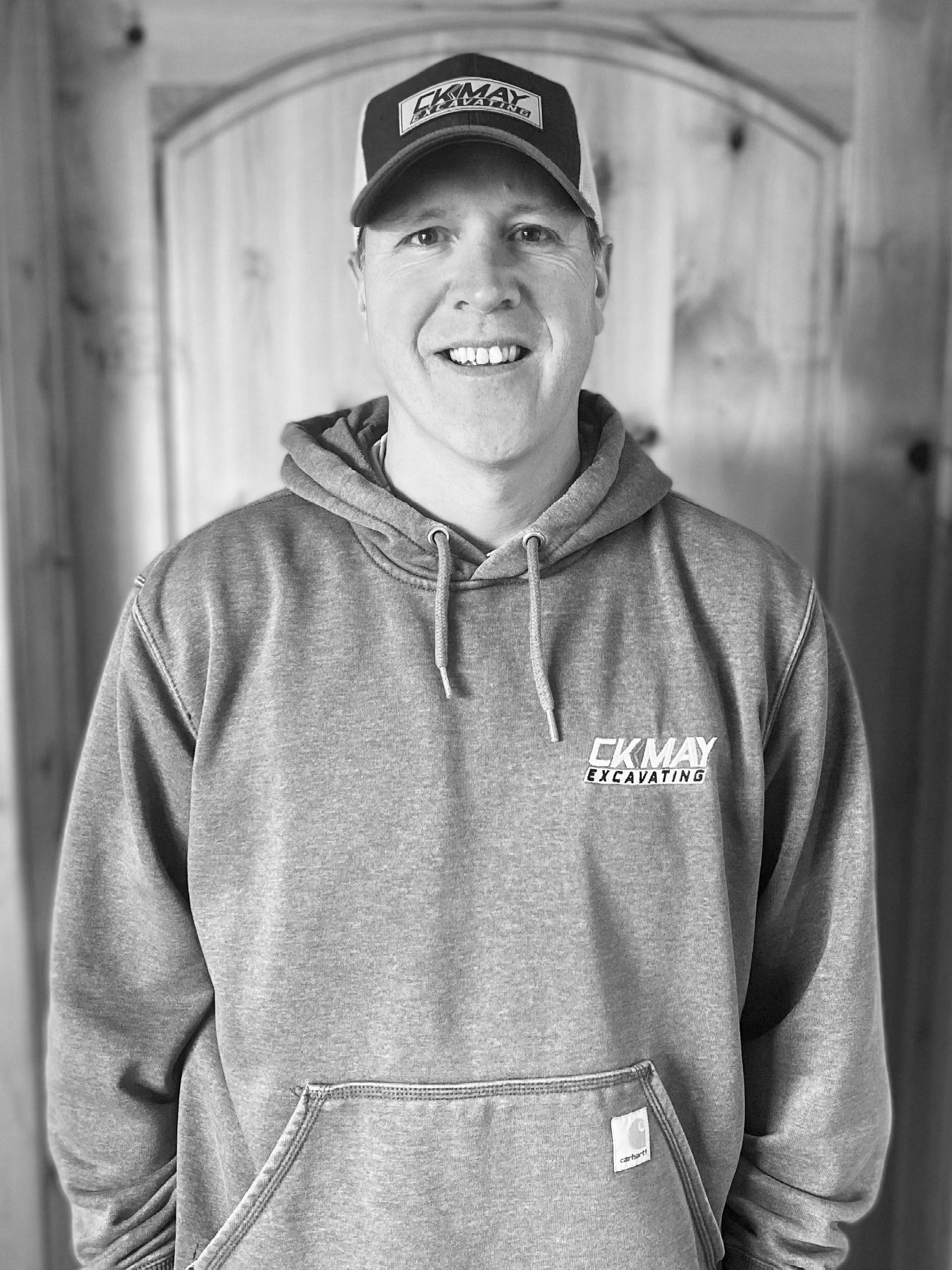 A man wearing a hoodie and a hat is smiling in a black and white photo.