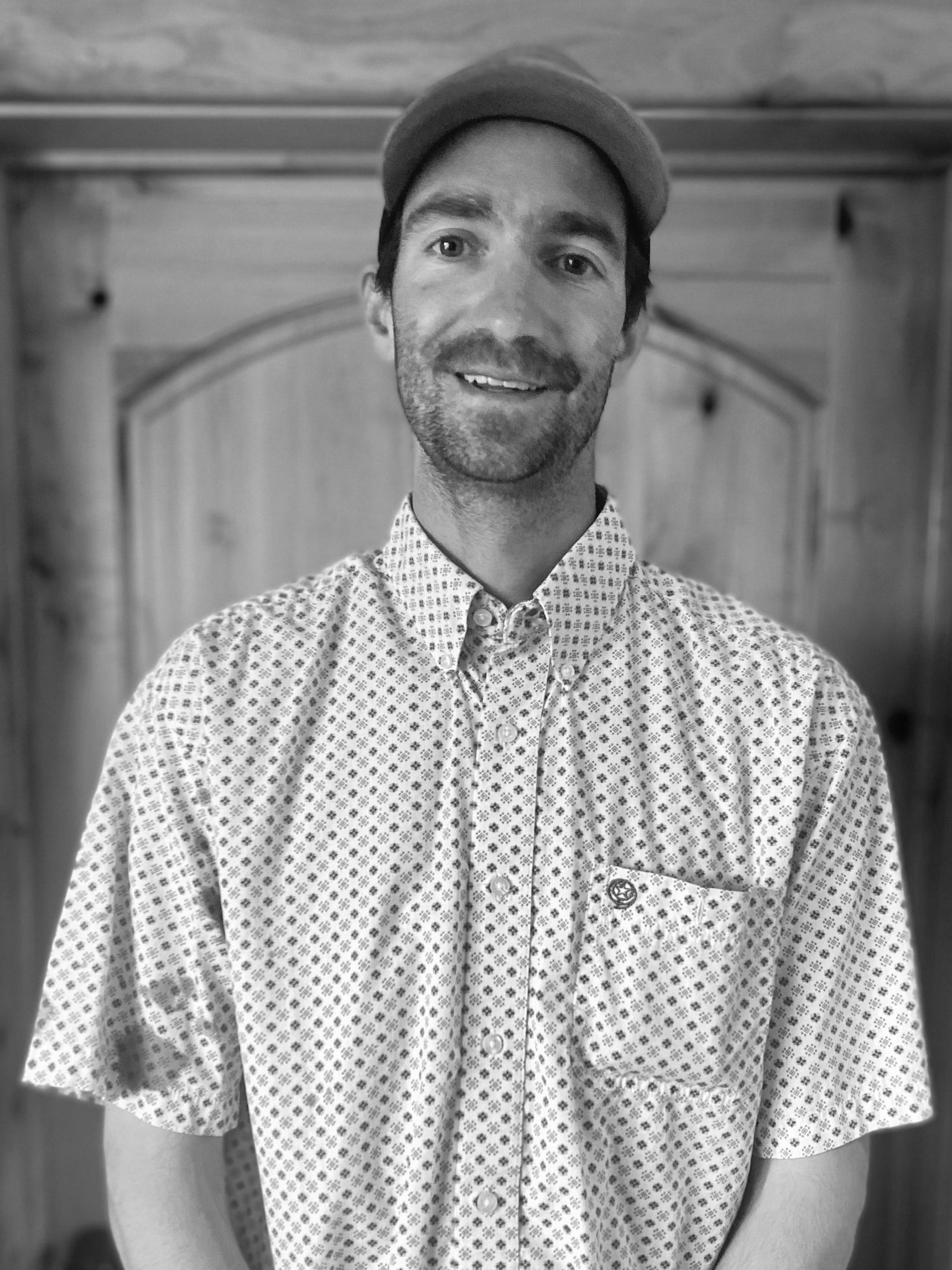 A man wearing a hat and a shirt is smiling in a black and white photo.