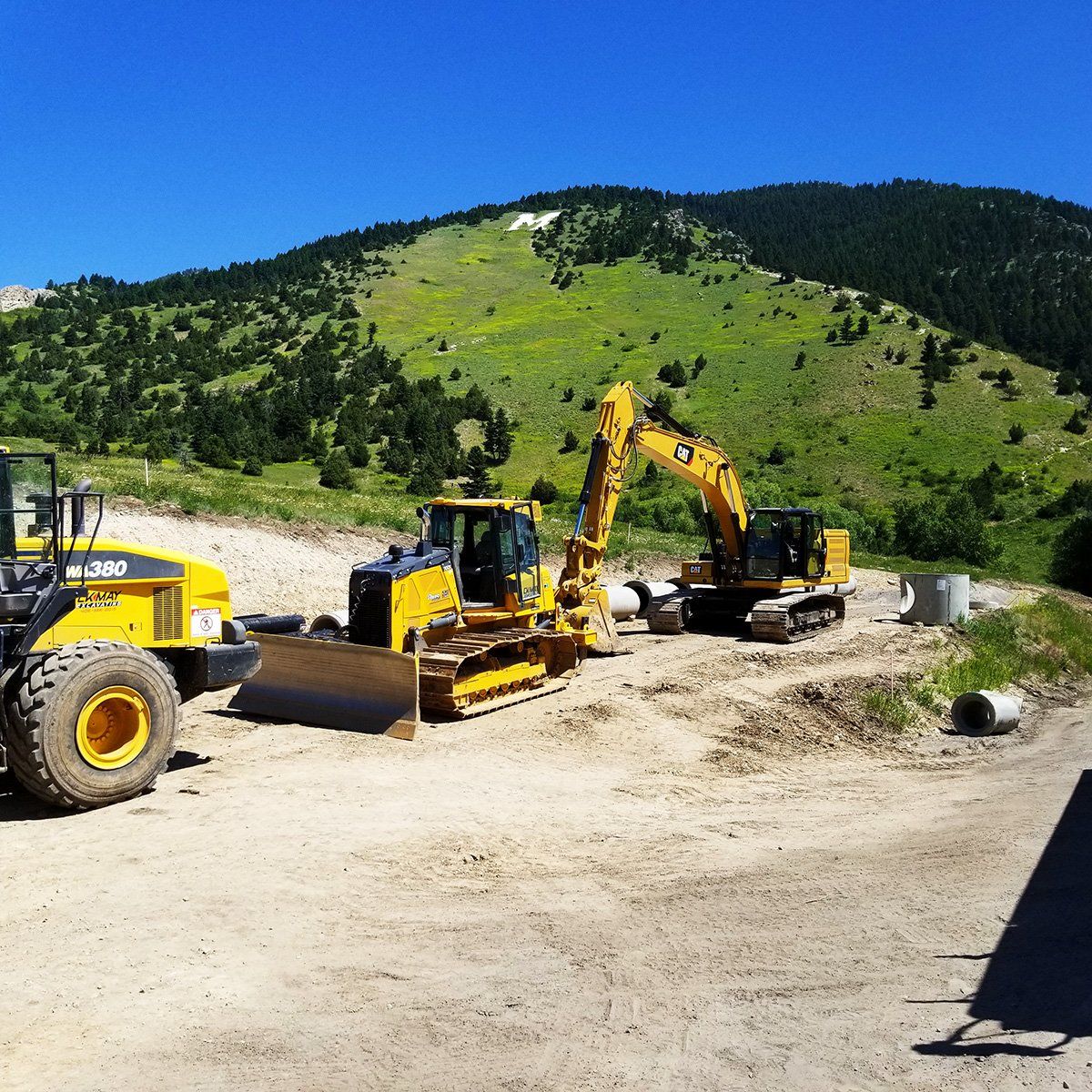 A bulldozer and an excavator are parked in a dirt field with mountains in the background