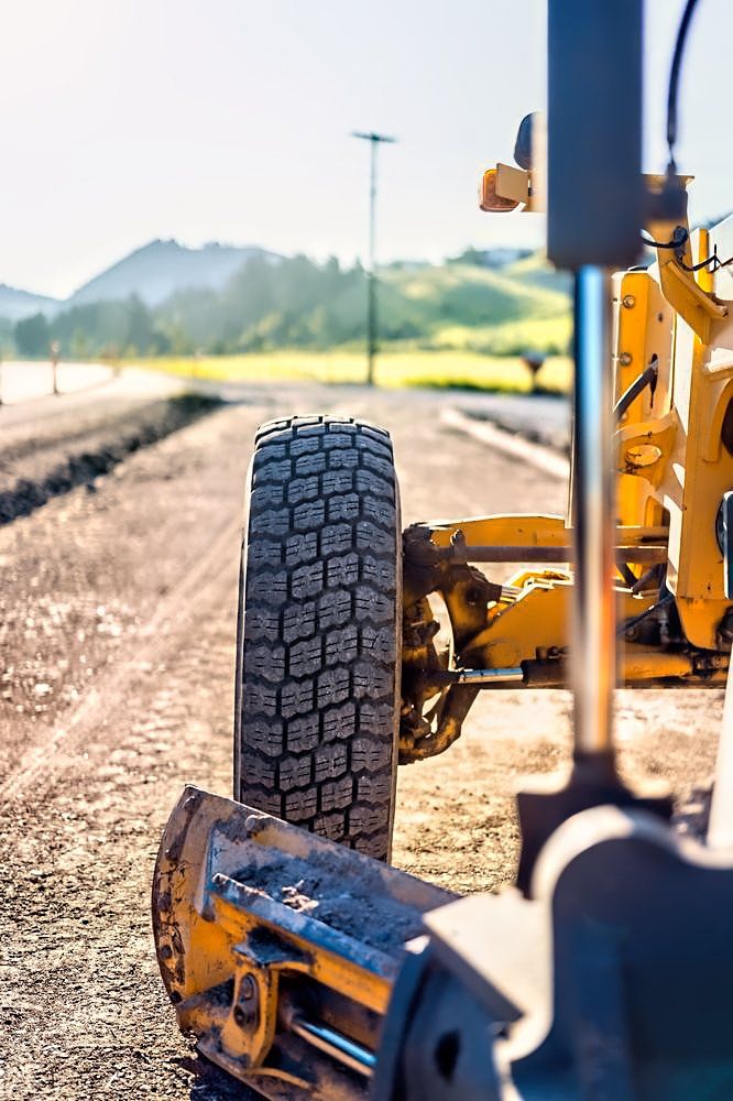 A yellow tractor is working on a dirt road.