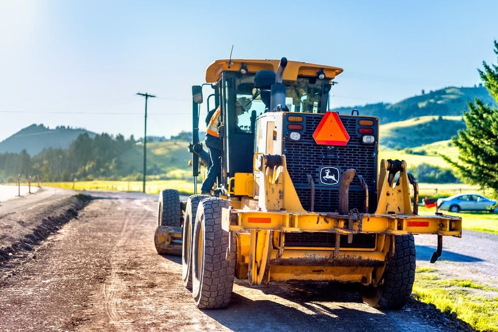 A yellow tractor is driving down a dirt road.