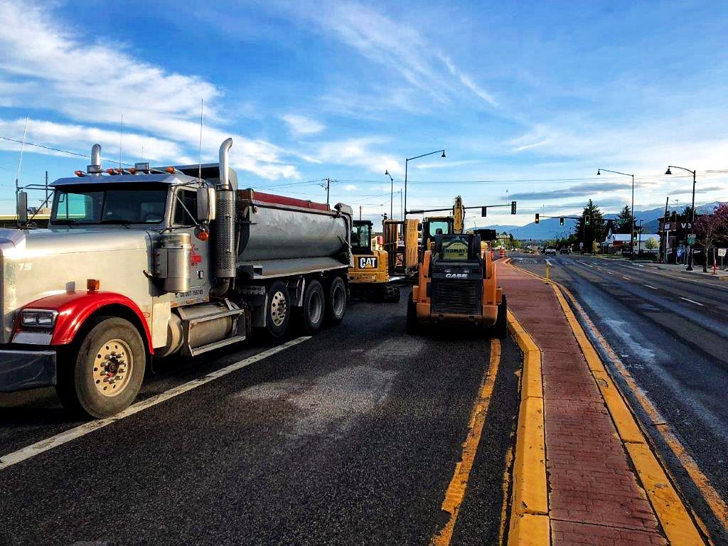 A semi truck is parked on the side of the road next to a bulldozer.
