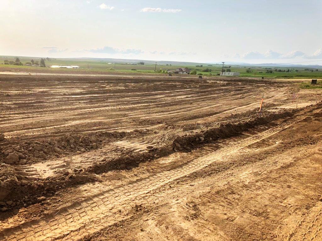 A dirt road going through a muddy field with a farm in the background.