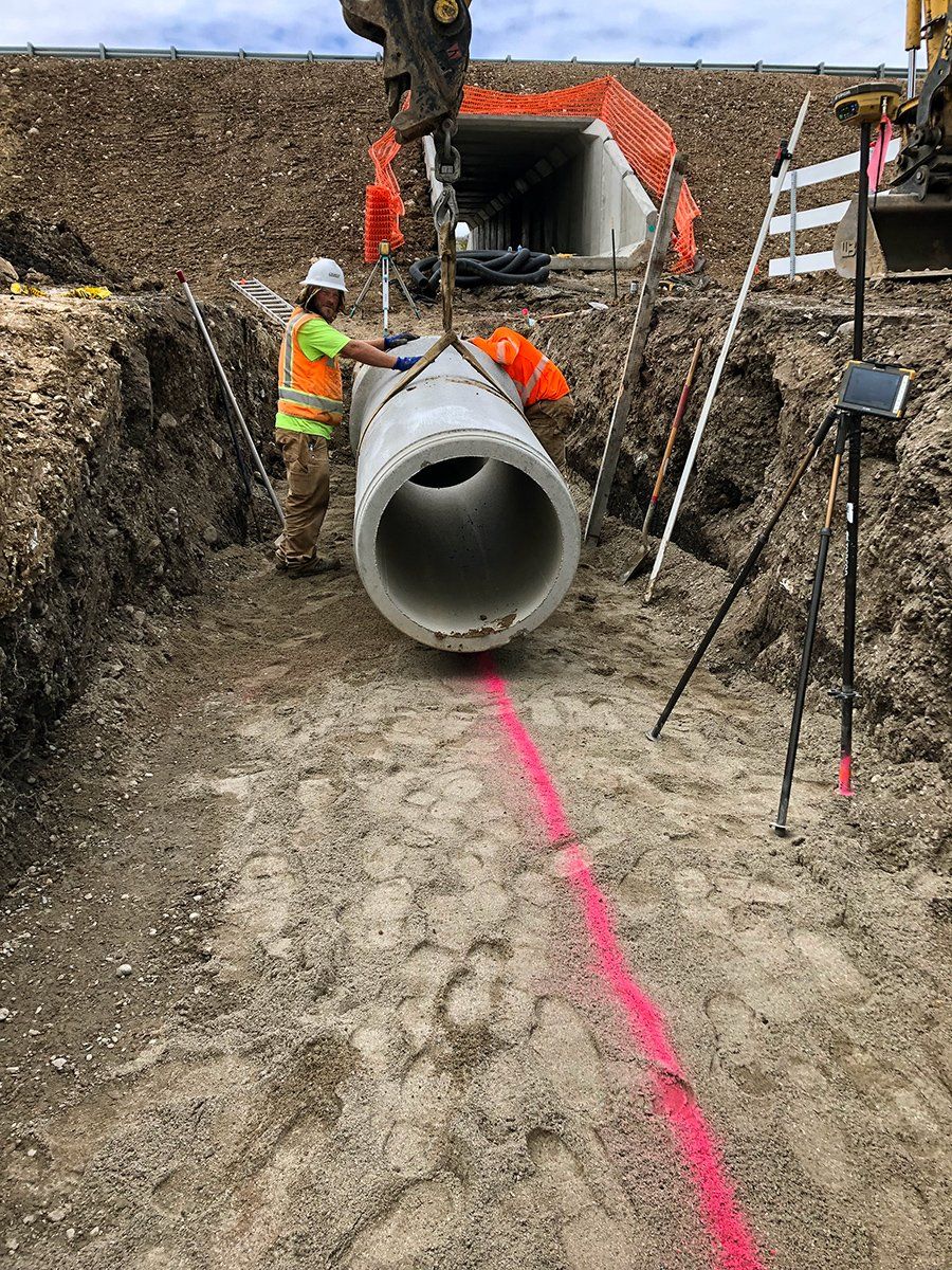 A man is lifting a large pipe in the dirt.