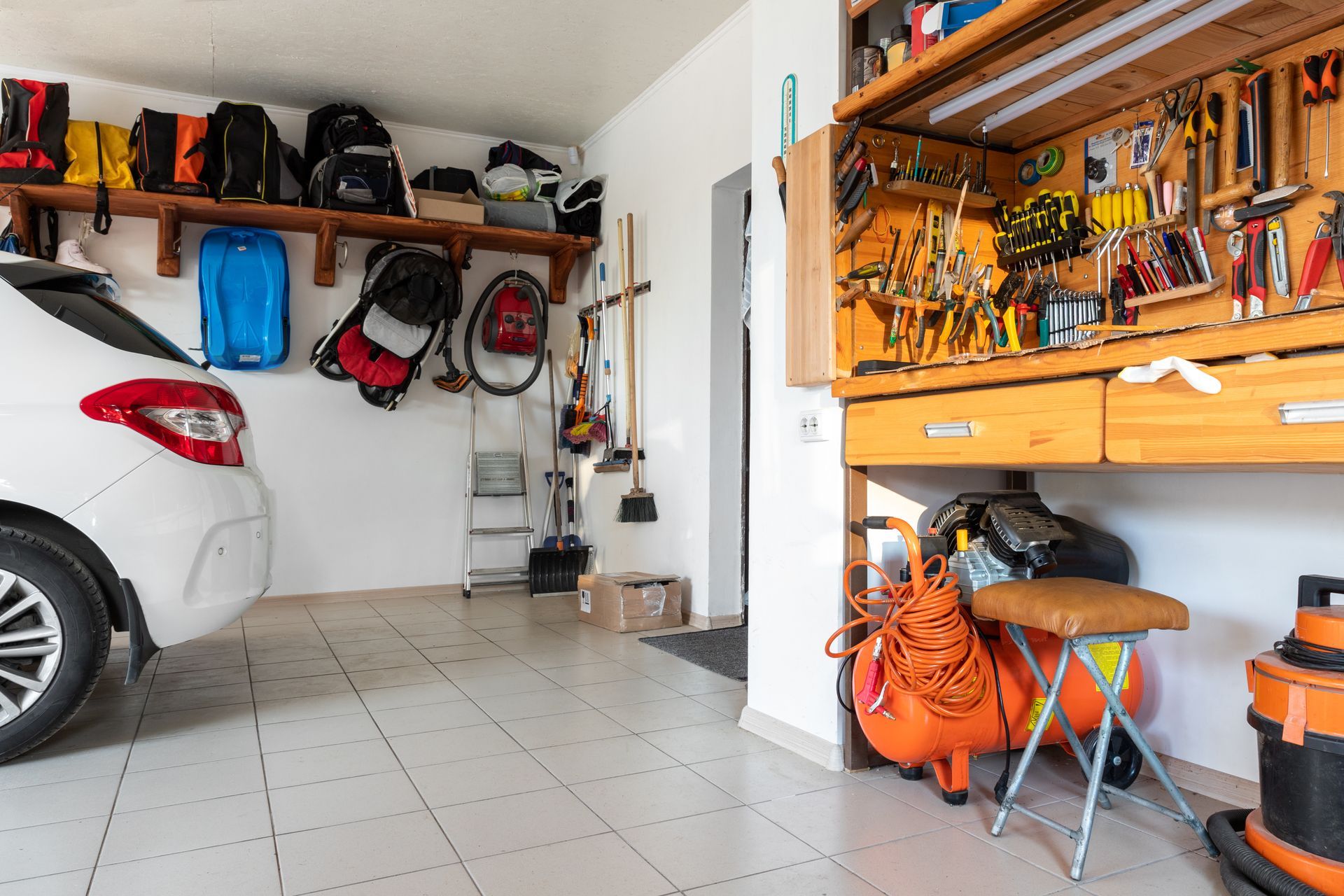 Garage interior with white car, tool bench, and storage shelves.