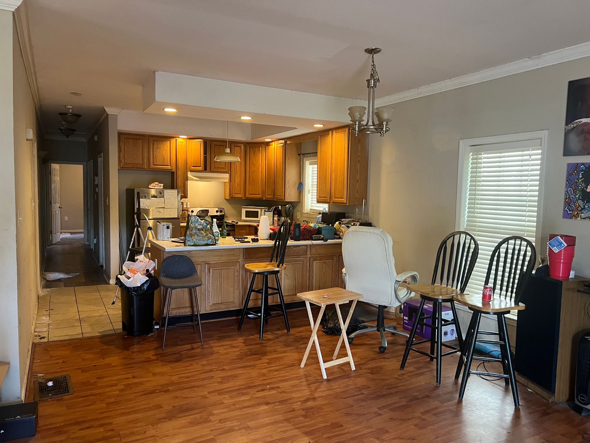 A living room with wooden floors and a kitchen in the background.