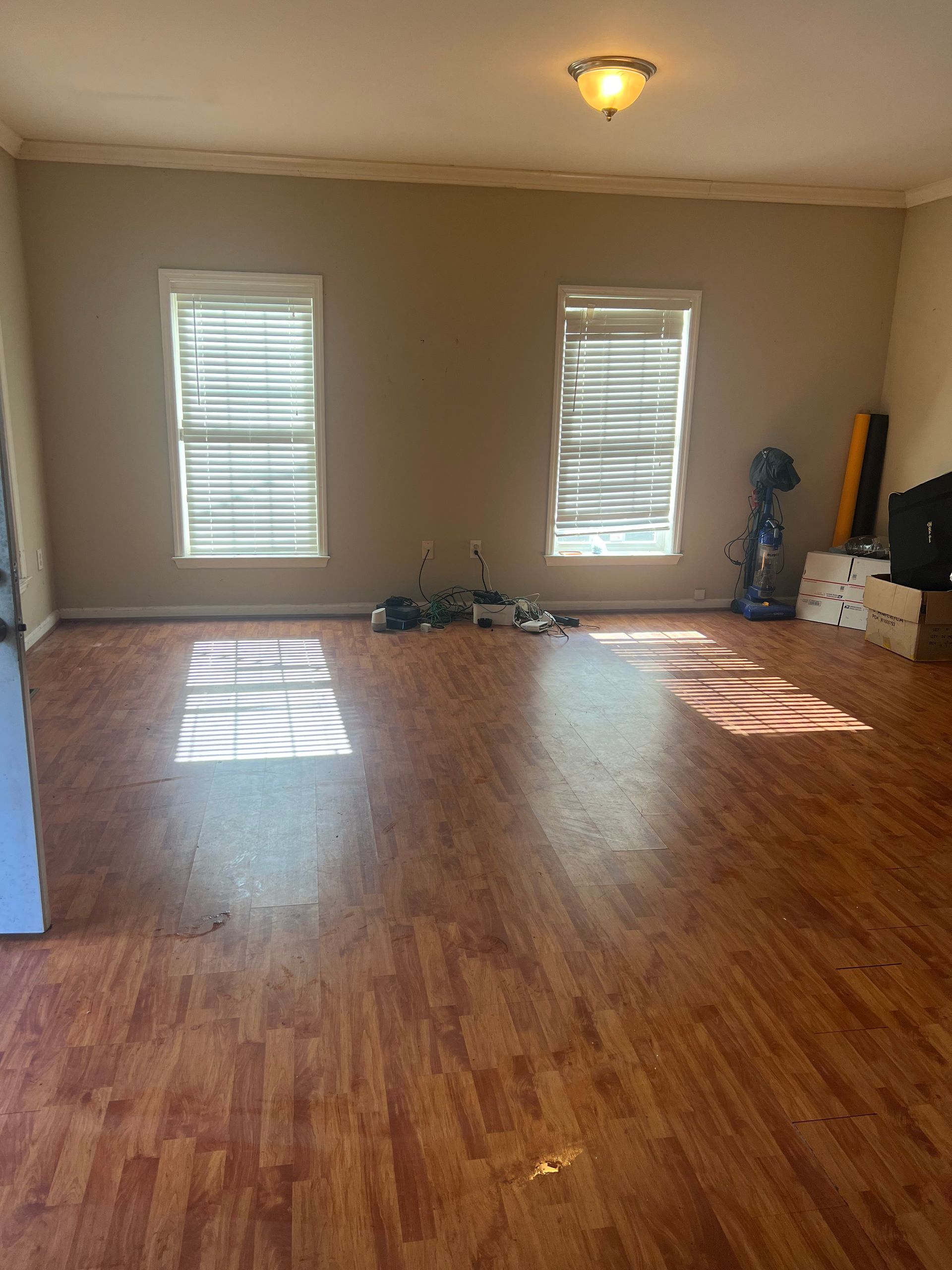 An empty living room with hardwood floors and two windows.