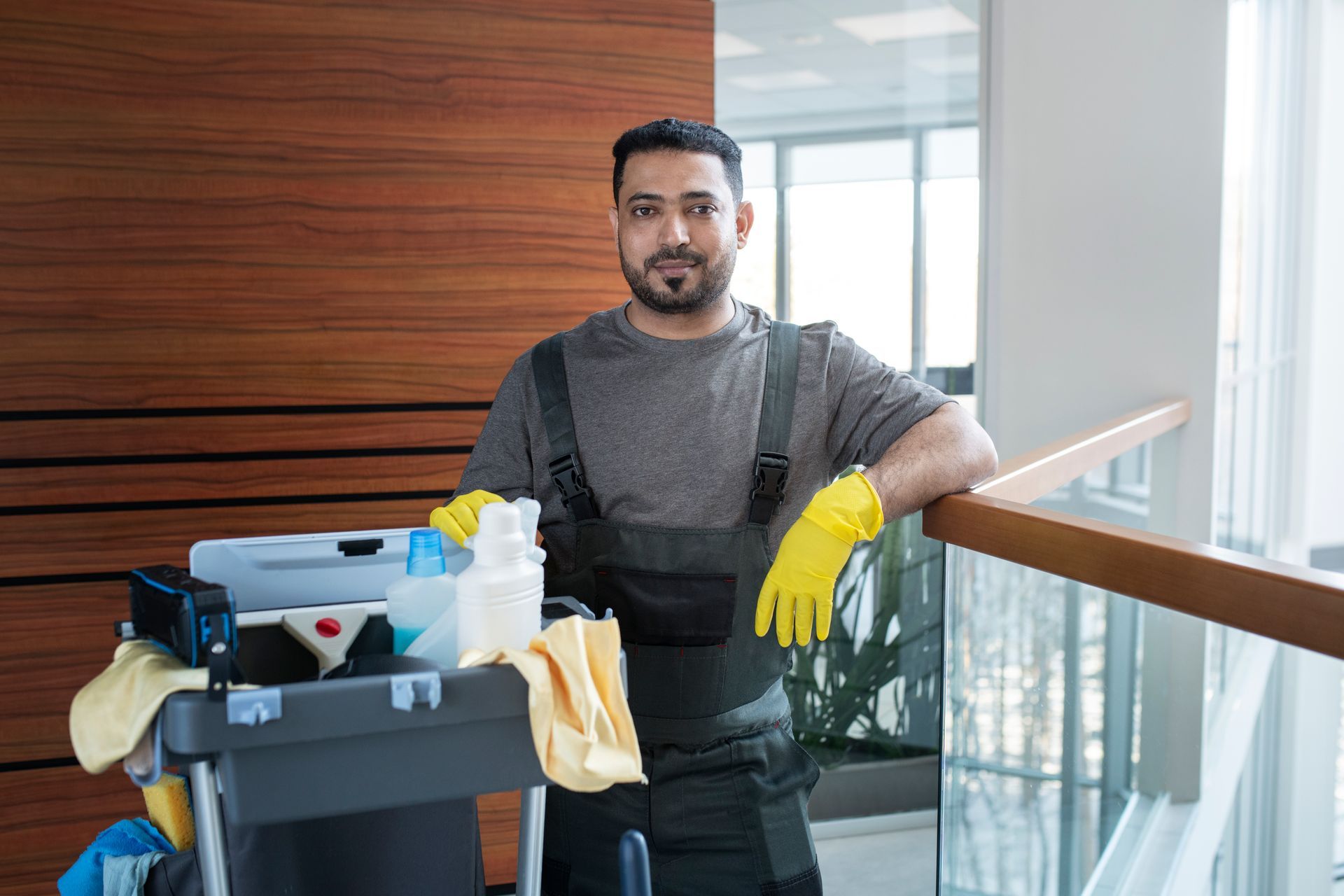 A man is leaning on a railing while holding a cleaning cart.