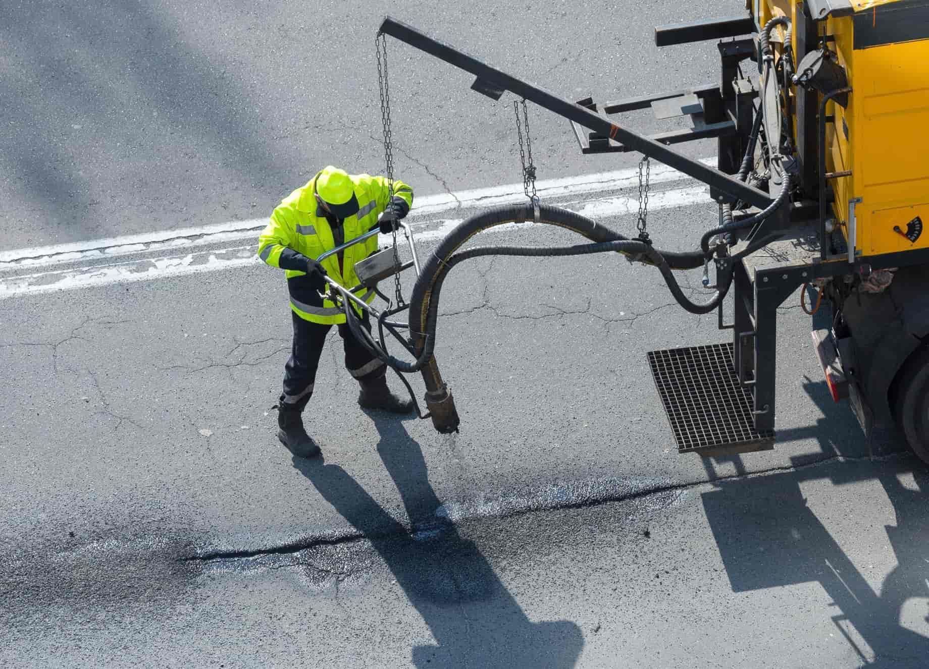 A man in a yellow jacket is working on a road next to a yellow truck — BB & F Constructions Pty Ltd In Wingham, NSW