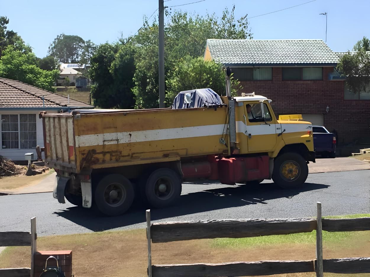 A Yellow Dump Truck Is Parked In Front Of A House — BB & F Constructions Pty Ltd In Taree, NSW