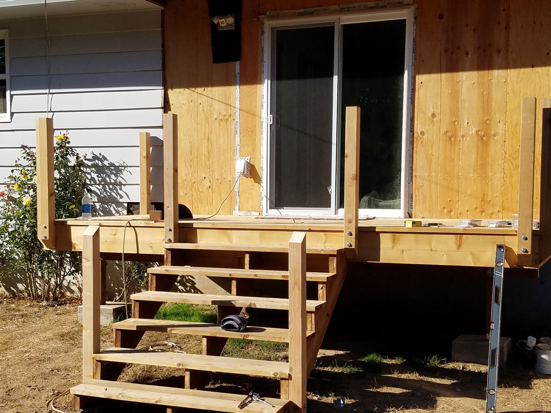 Wooden deck with steps leading to a sliding glass door. The exterior of a building is under construction.