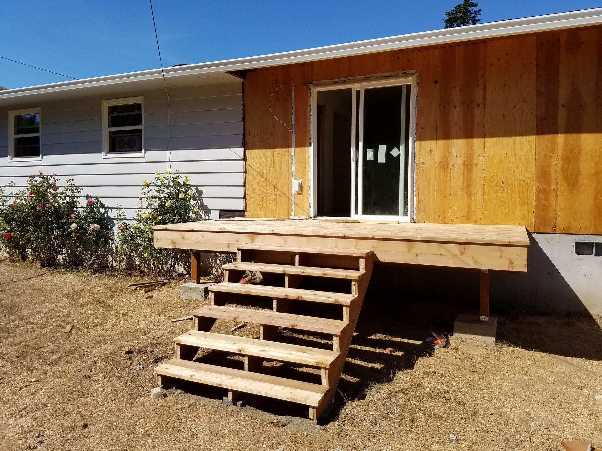 Wooden deck and stairs leading to a doorway, adjacent to a light blue house.