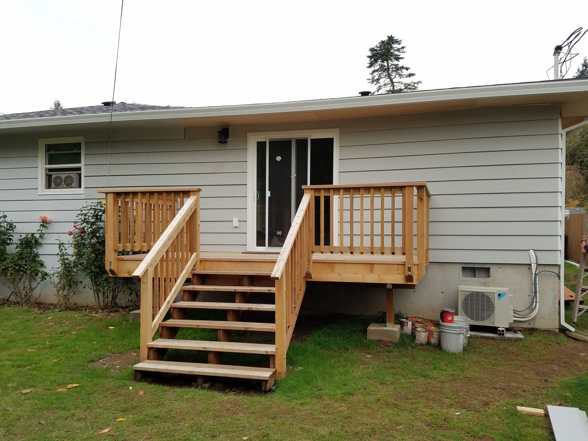 Wooden deck with stairs leading to a sliding glass door of a house with gray siding.