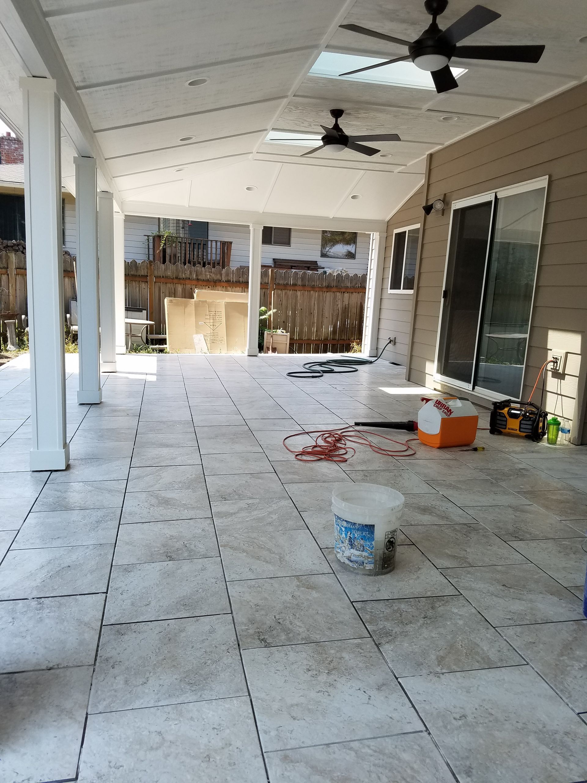 Covered patio under construction with white columns, light-colored tiles, and ceiling fans.