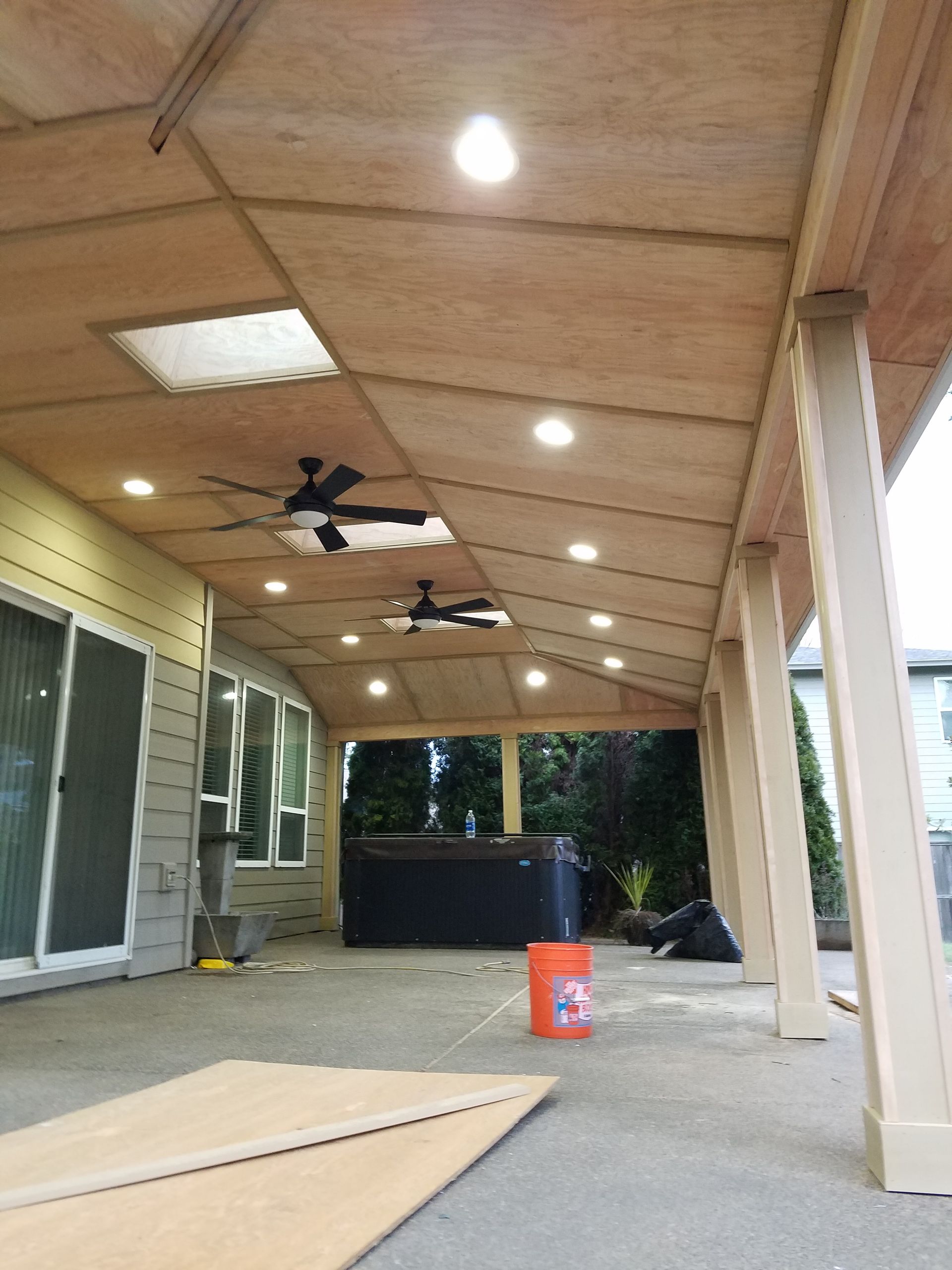 Covered patio with recessed lights and ceiling fans, overlooking a backyard with a hot tub.