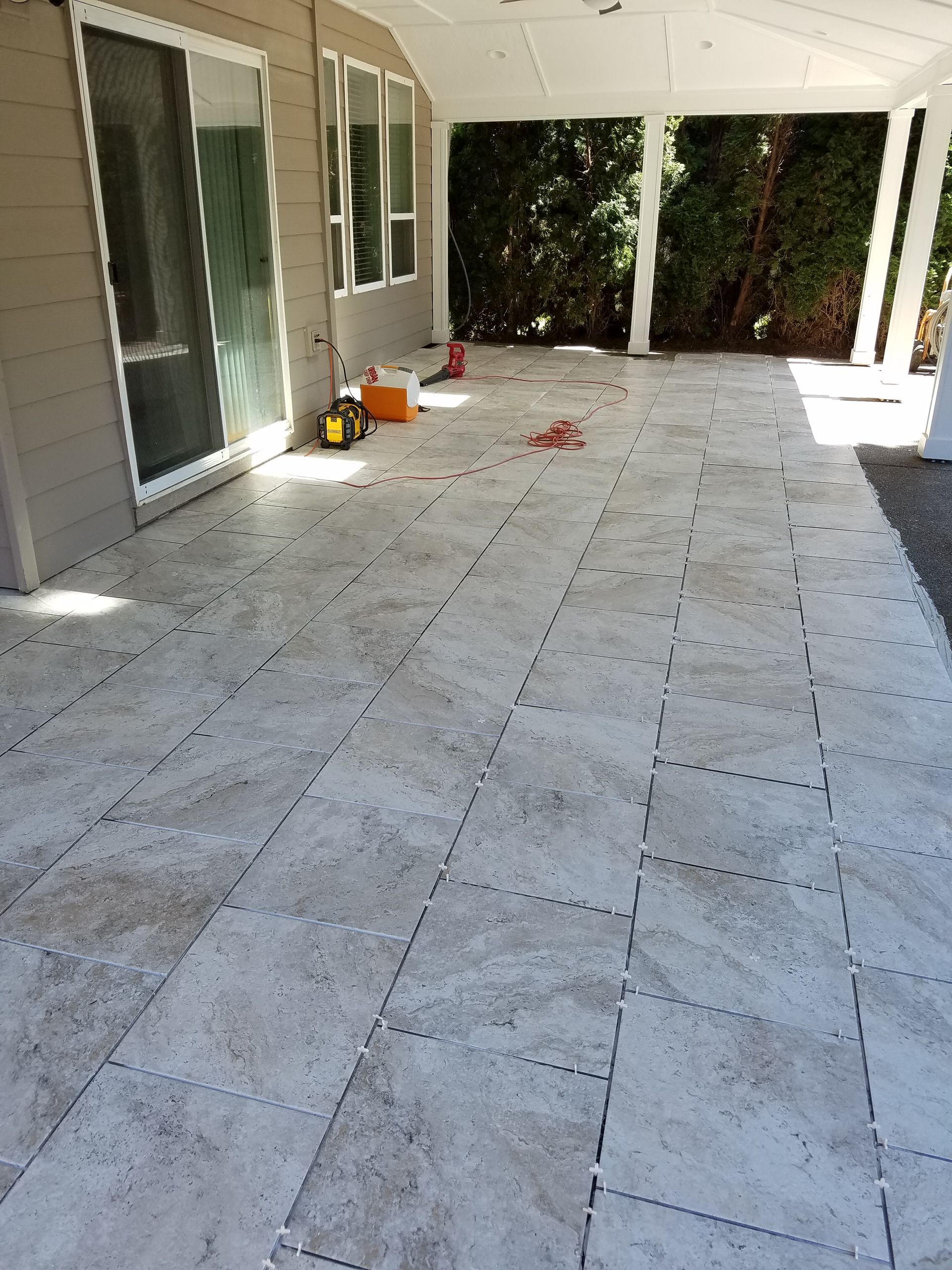 Patio with light-colored tiled floor under a covered porch. Sliding glass door and white columns are visible.