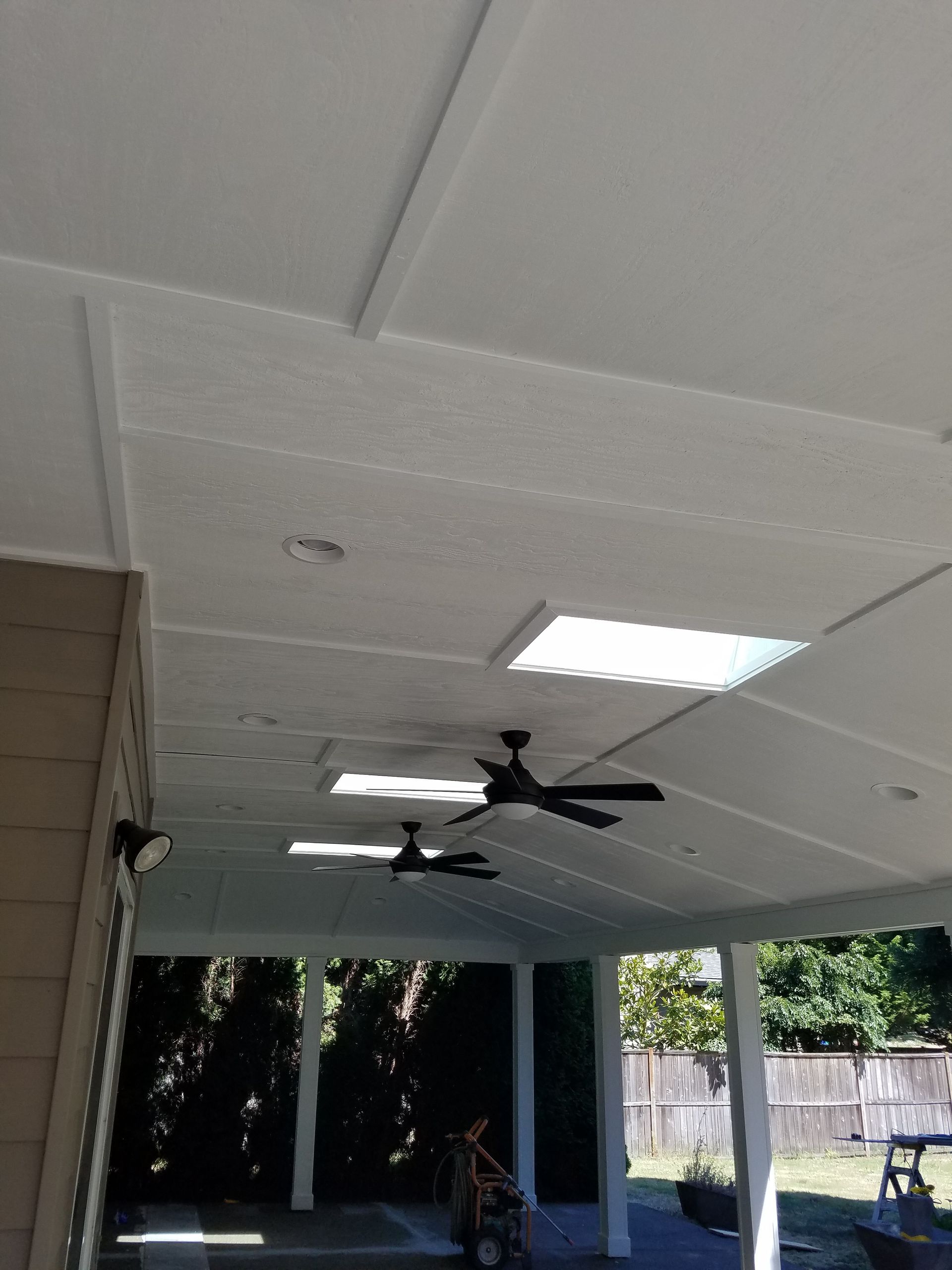 Covered patio ceiling with white panels, skylights, and ceiling fans.