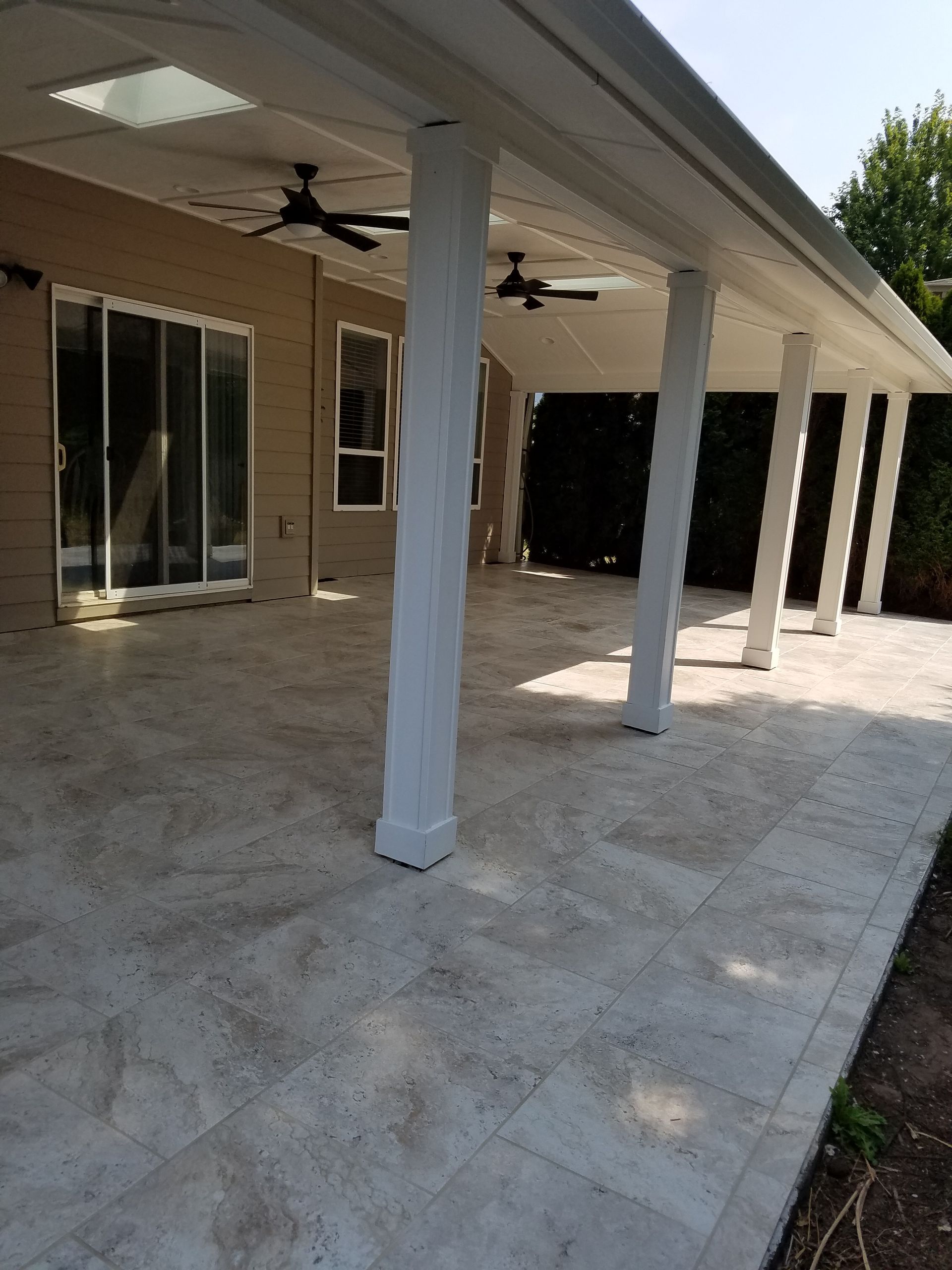 Covered patio with white pillars, beige tile floor, ceiling fans, and sliding glass doors.