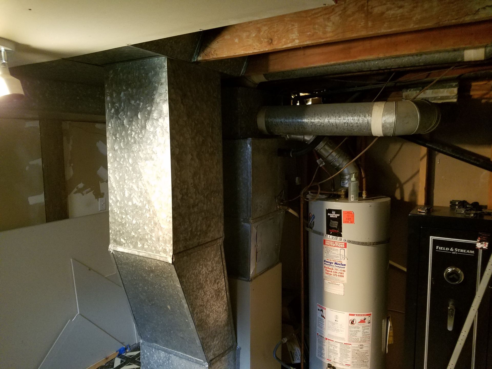 Ductwork and water heater in a basement. Galvanized steel ducts, water heater with exhaust pipe, and safe are visible.