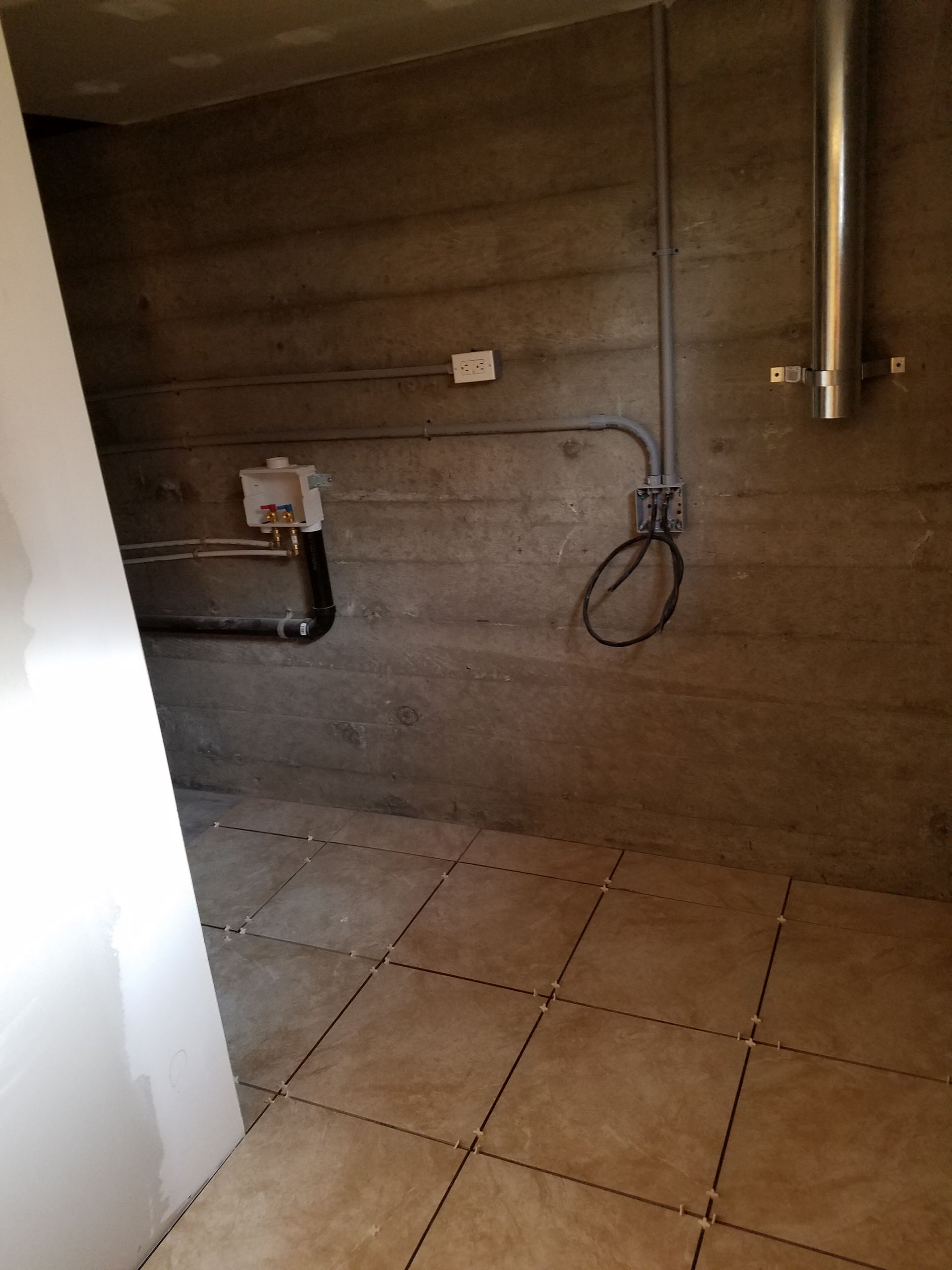 Basement room with concrete walls, tiled floor, plumbing, and electrical conduits.