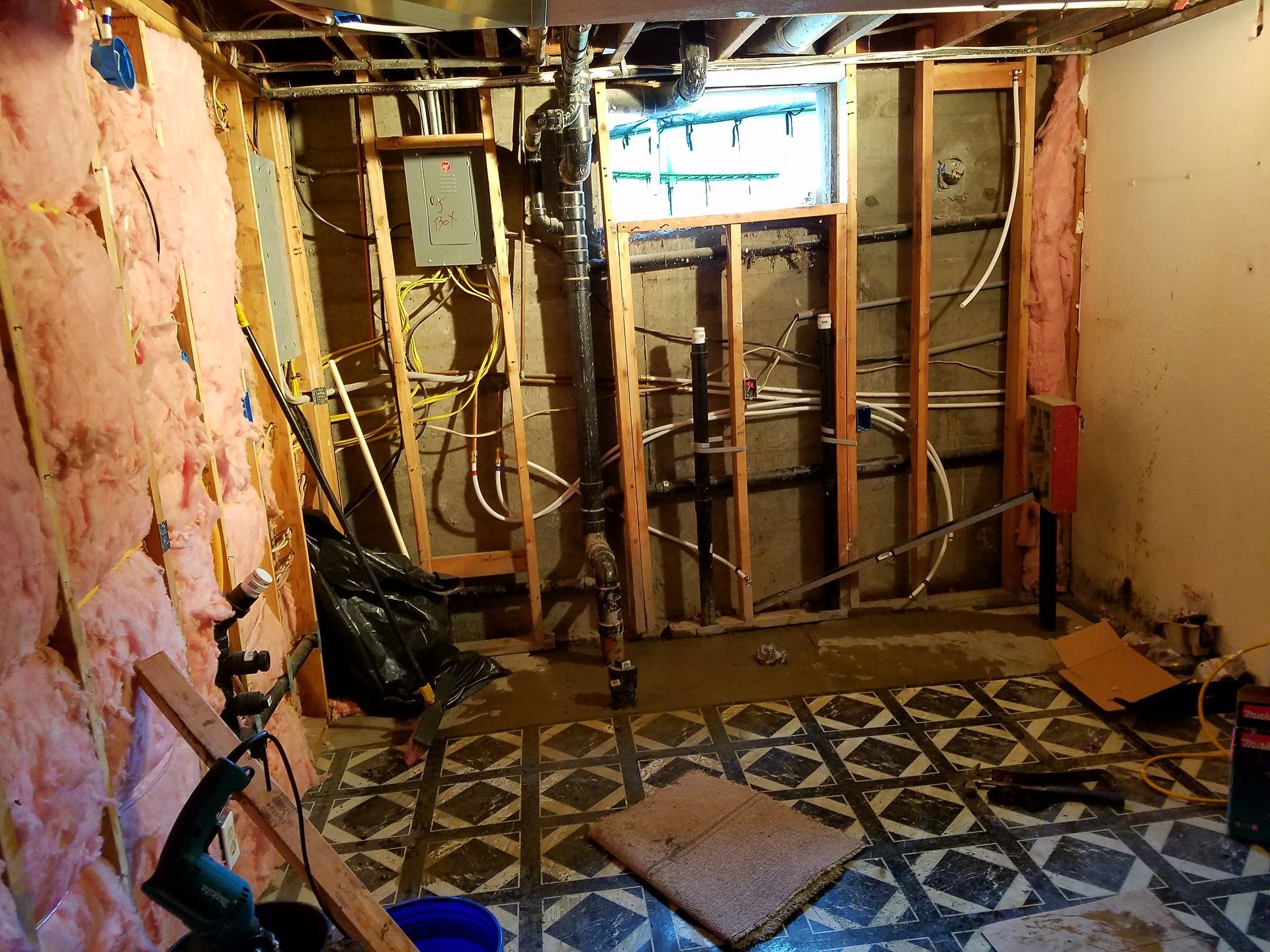 Basement interior under construction. Exposed framing, insulation, electrical wiring, and plumbing.