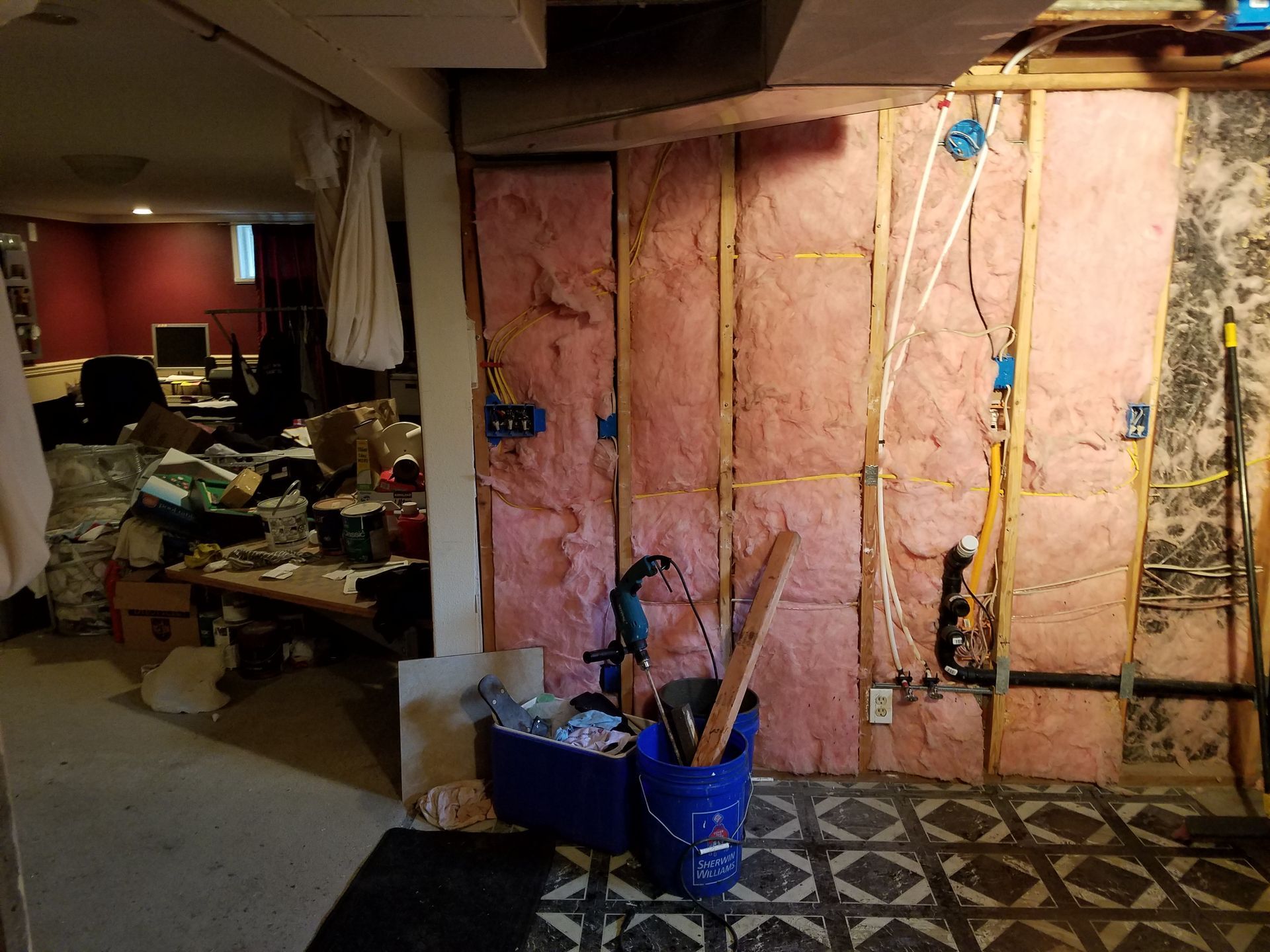 Basement interior with exposed insulation, electrical wiring, and a messy storage area.