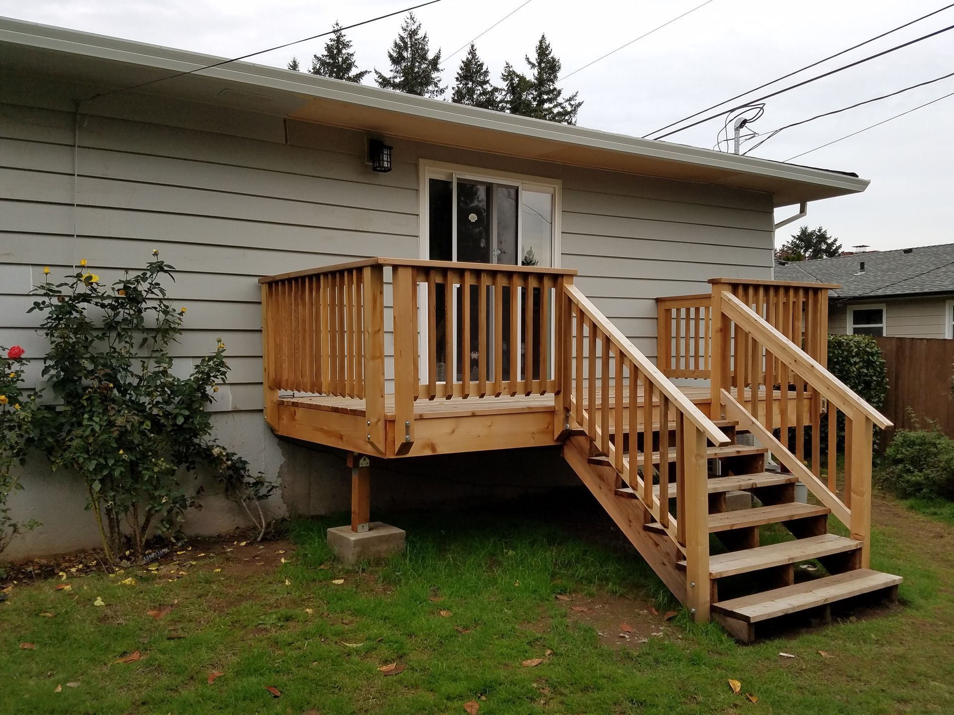Wooden deck with stairs leading to a house with a sliding glass door. Overcast sky.