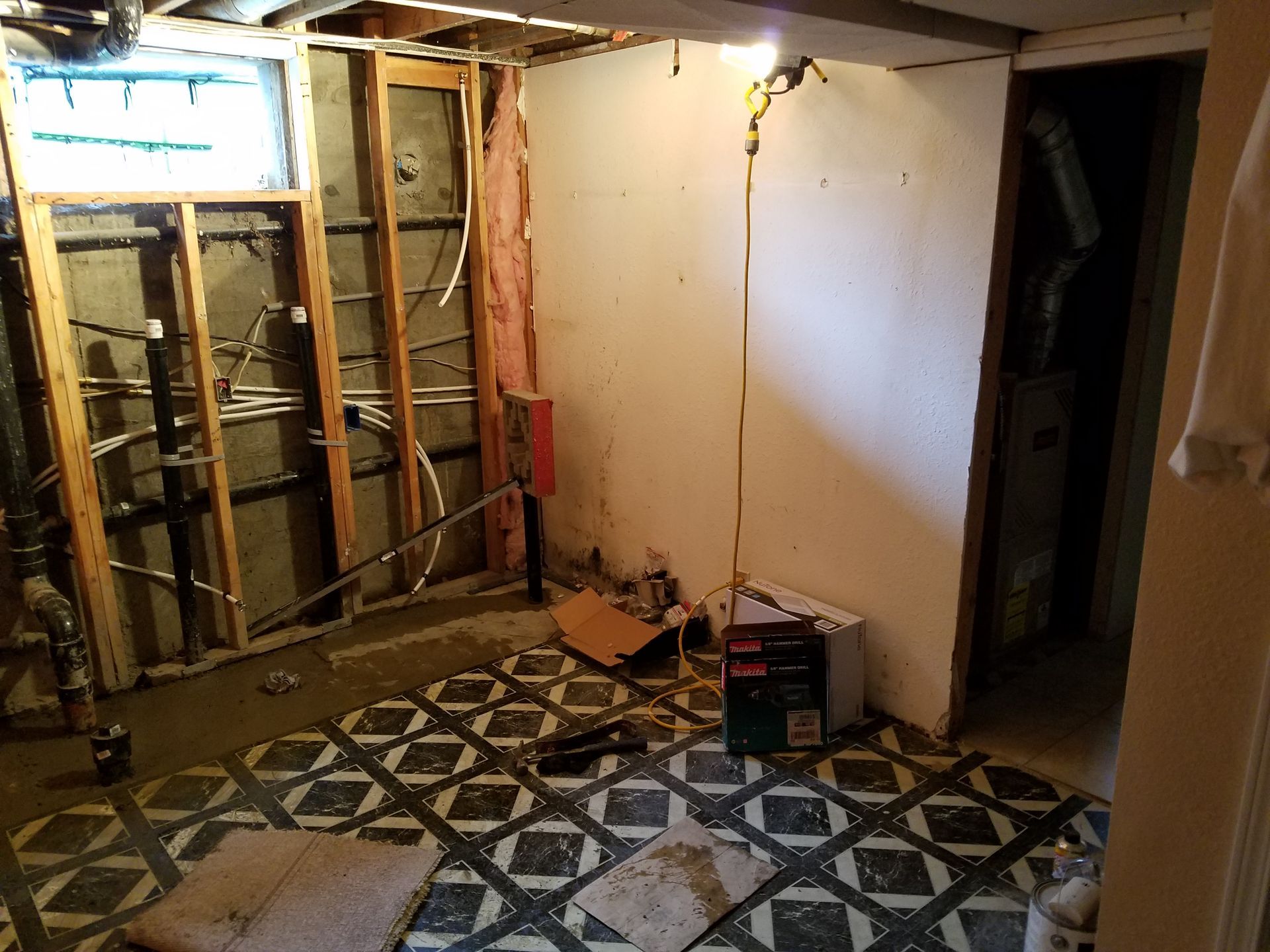 Basement renovation in progress. Exposed framing, pipes, and electrical wiring. Old patterned floor.