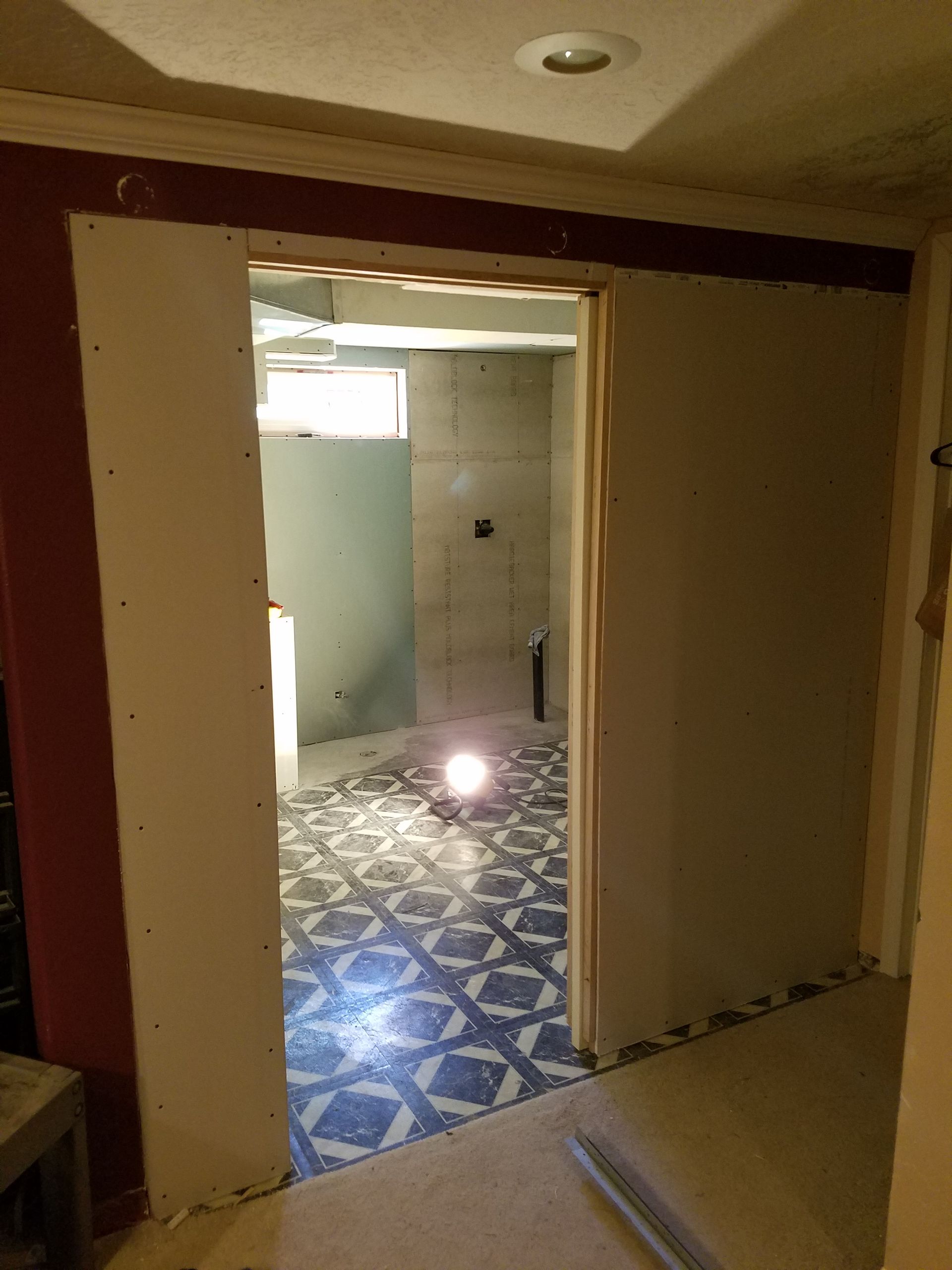 An open doorway with drywall framing leading into a bathroom with blue and white tile floors under construction.
