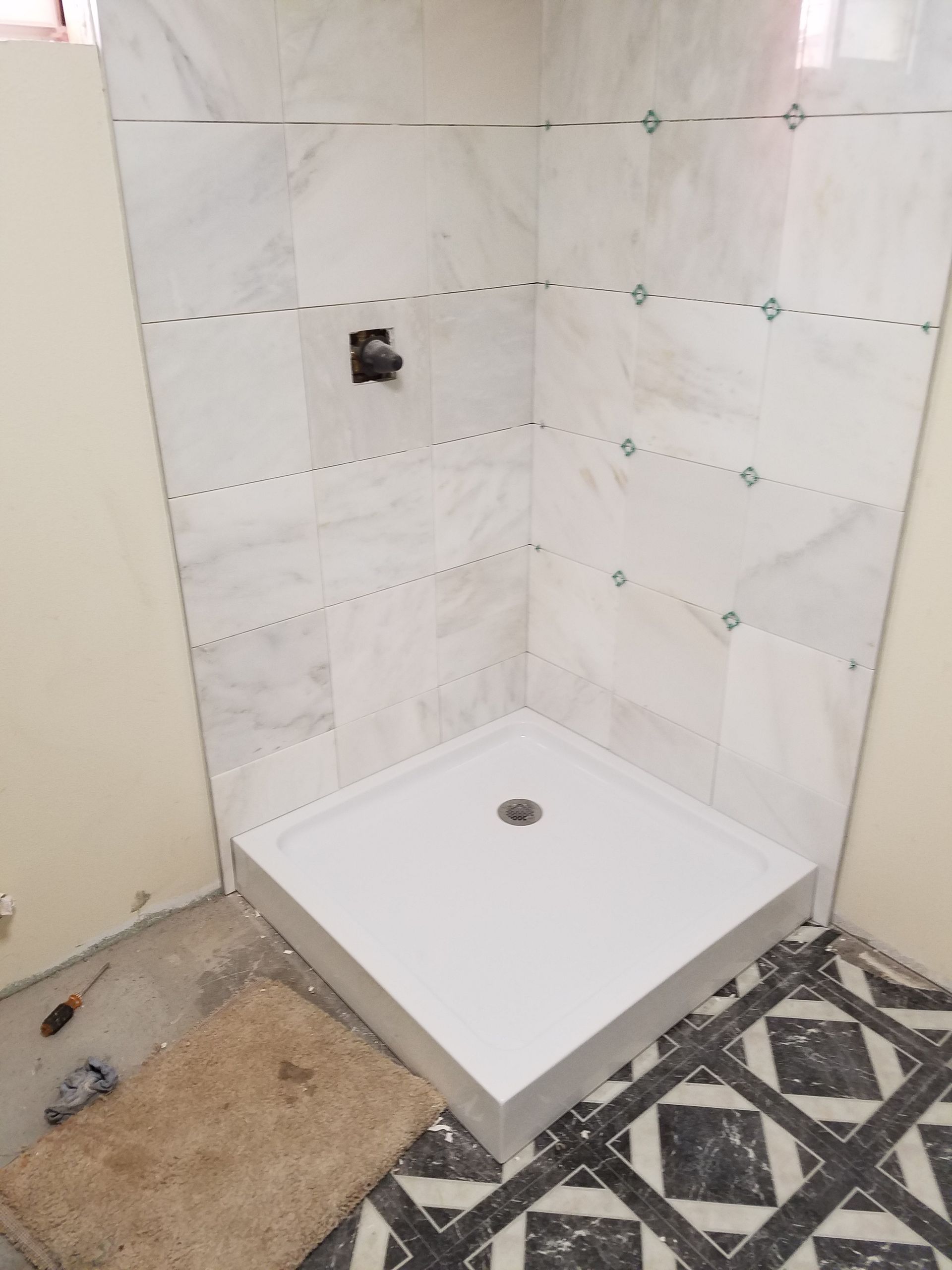 Corner shower stall with white base, marble tile walls, black faucet, in a room under construction.