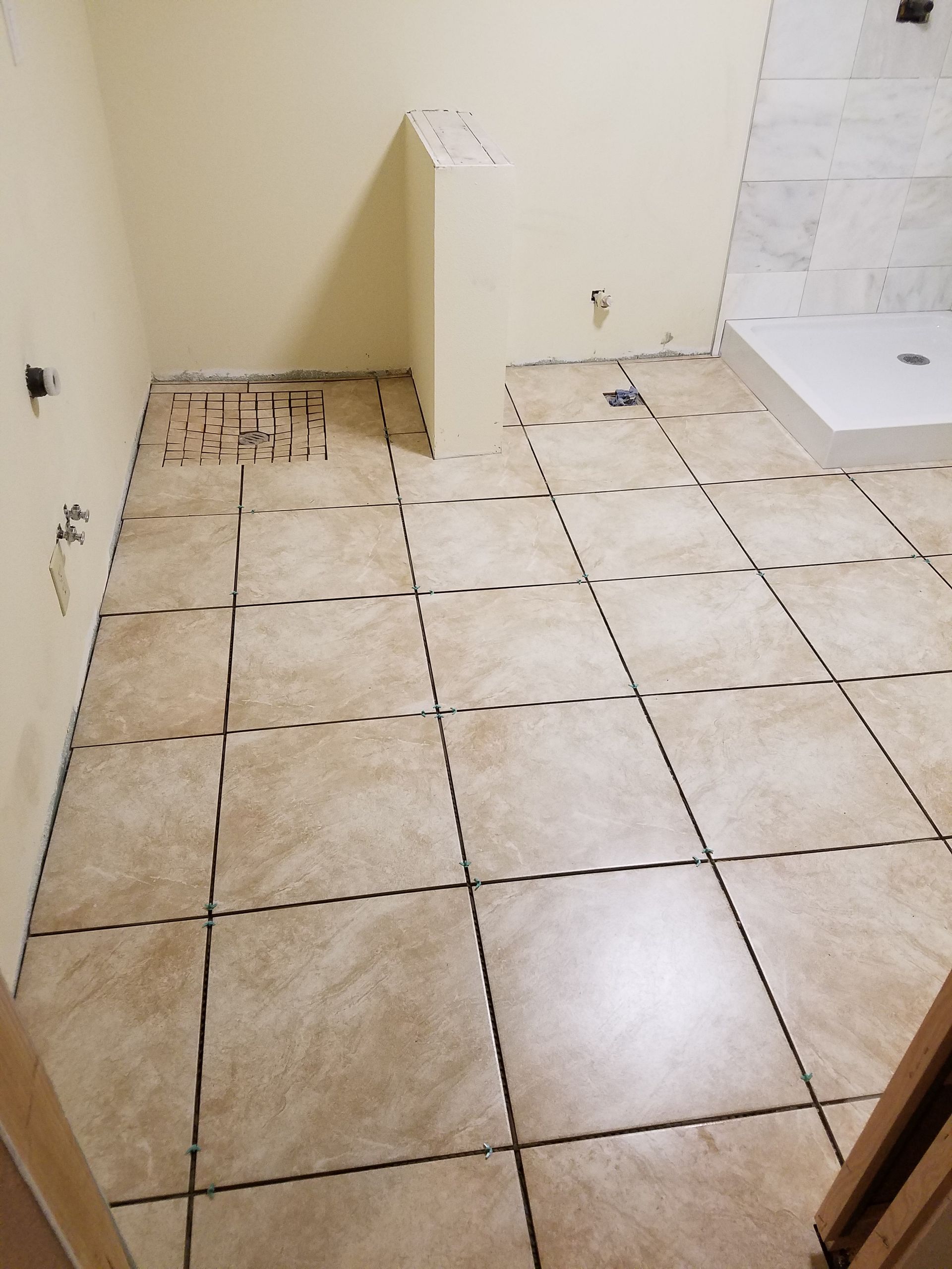 Bathroom with beige tile flooring partially laid; tan walls; white shower.