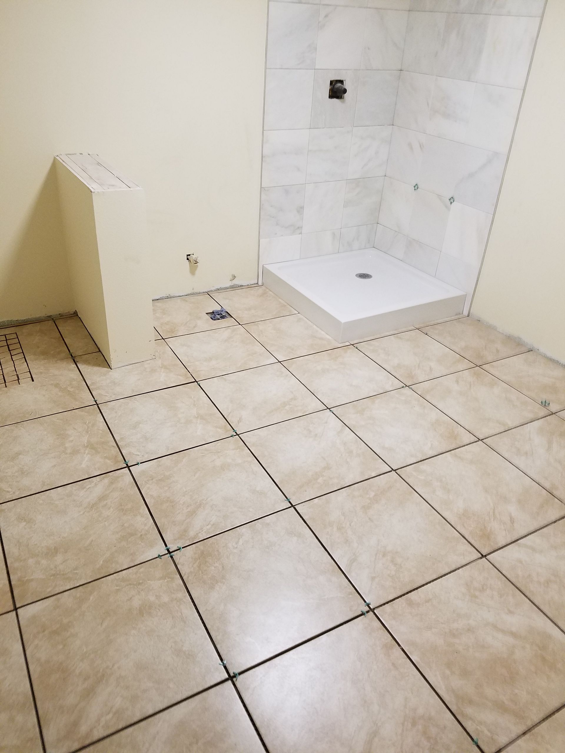 Bathroom under renovation with tile floor, white shower, and unfinished walls.