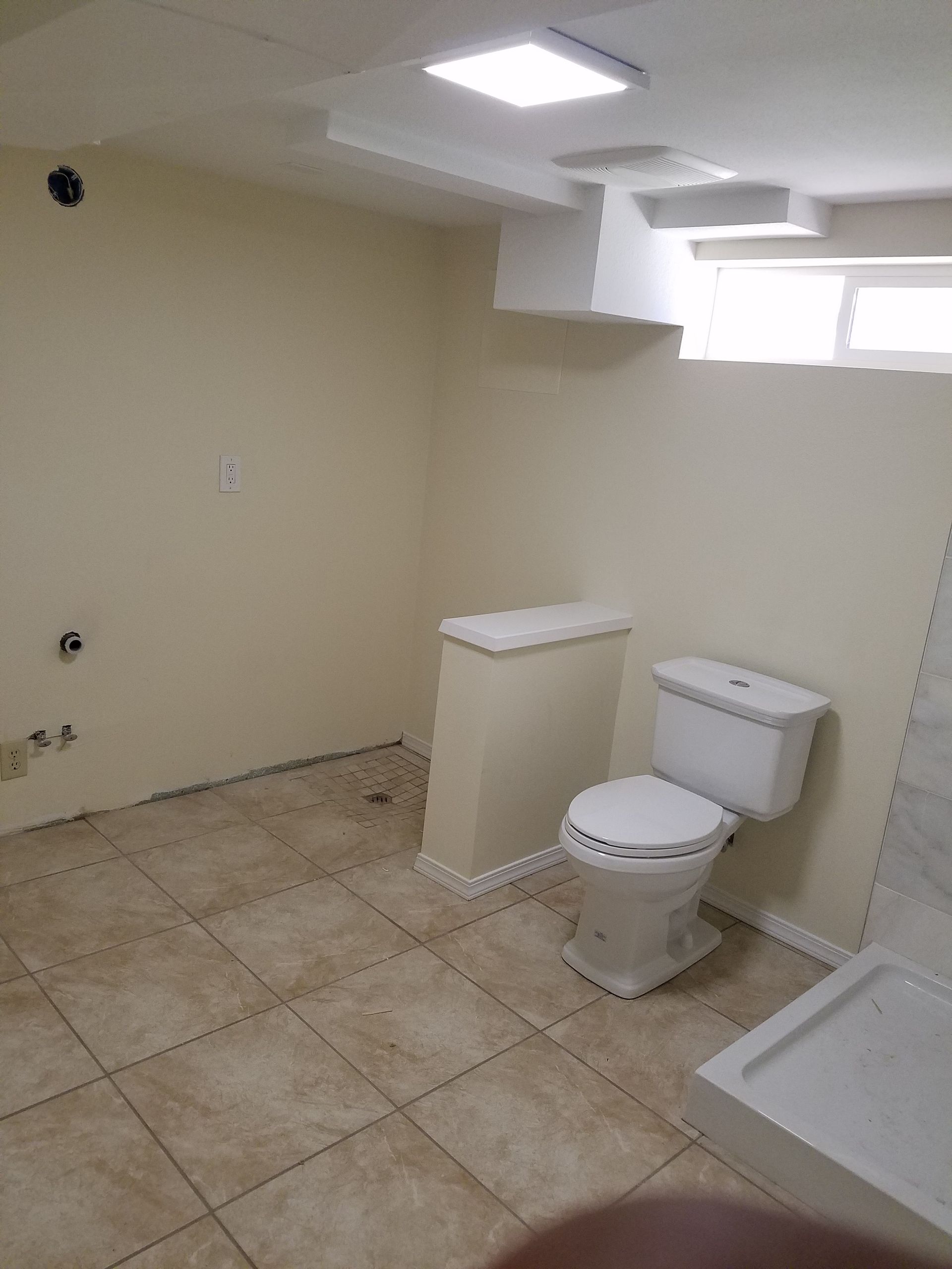 Bathroom with beige walls, tile floor, toilet, and shower base. Natural light from a window.
