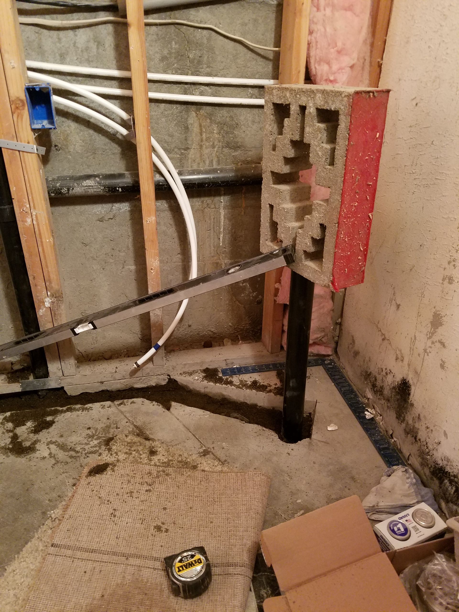 Construction site, basement: block structure on metal supports. Plumbing, insulation, and tape measure present.