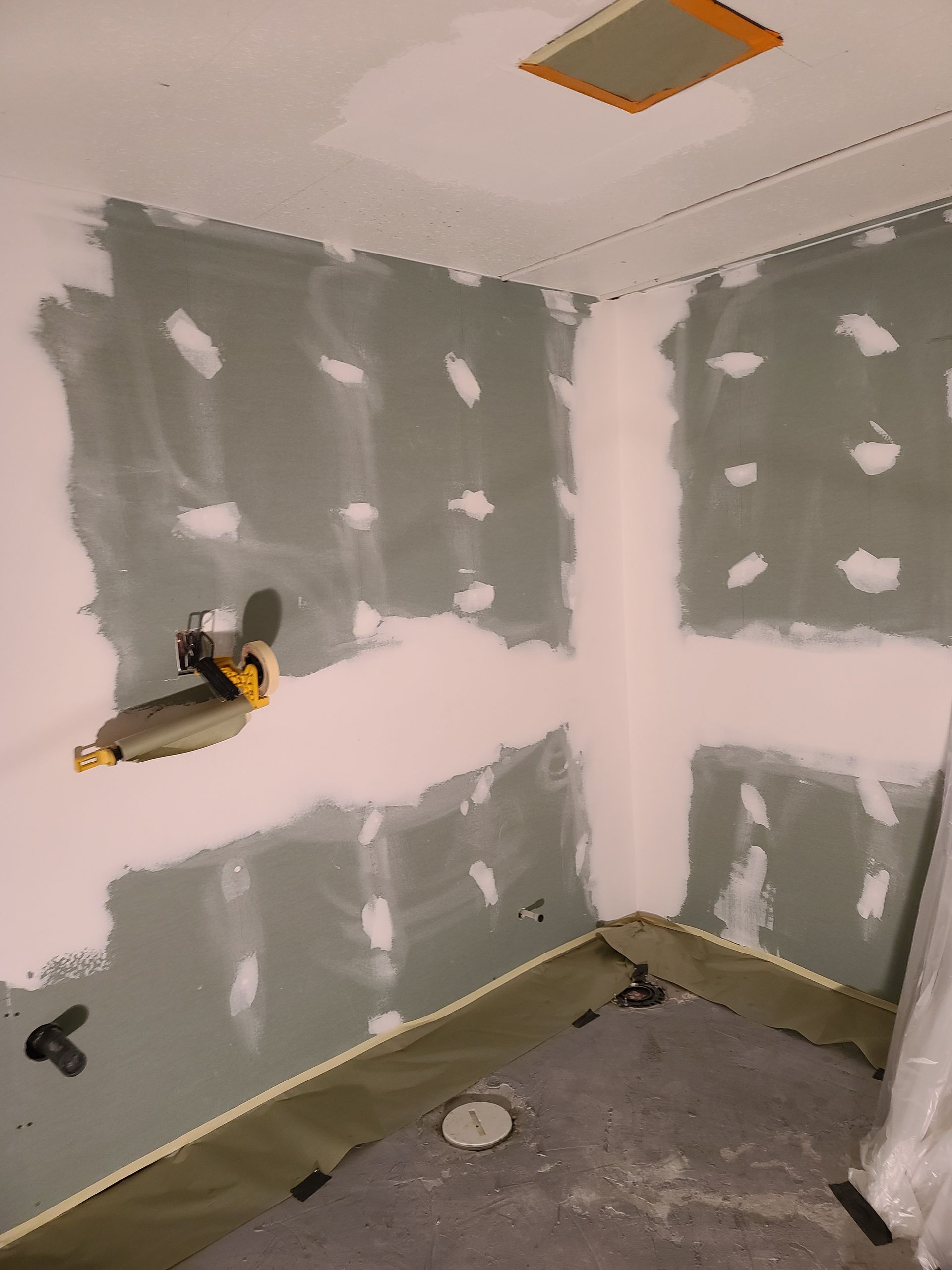 A corner room with drywall work in progress: green walls, white patching, and a work light.