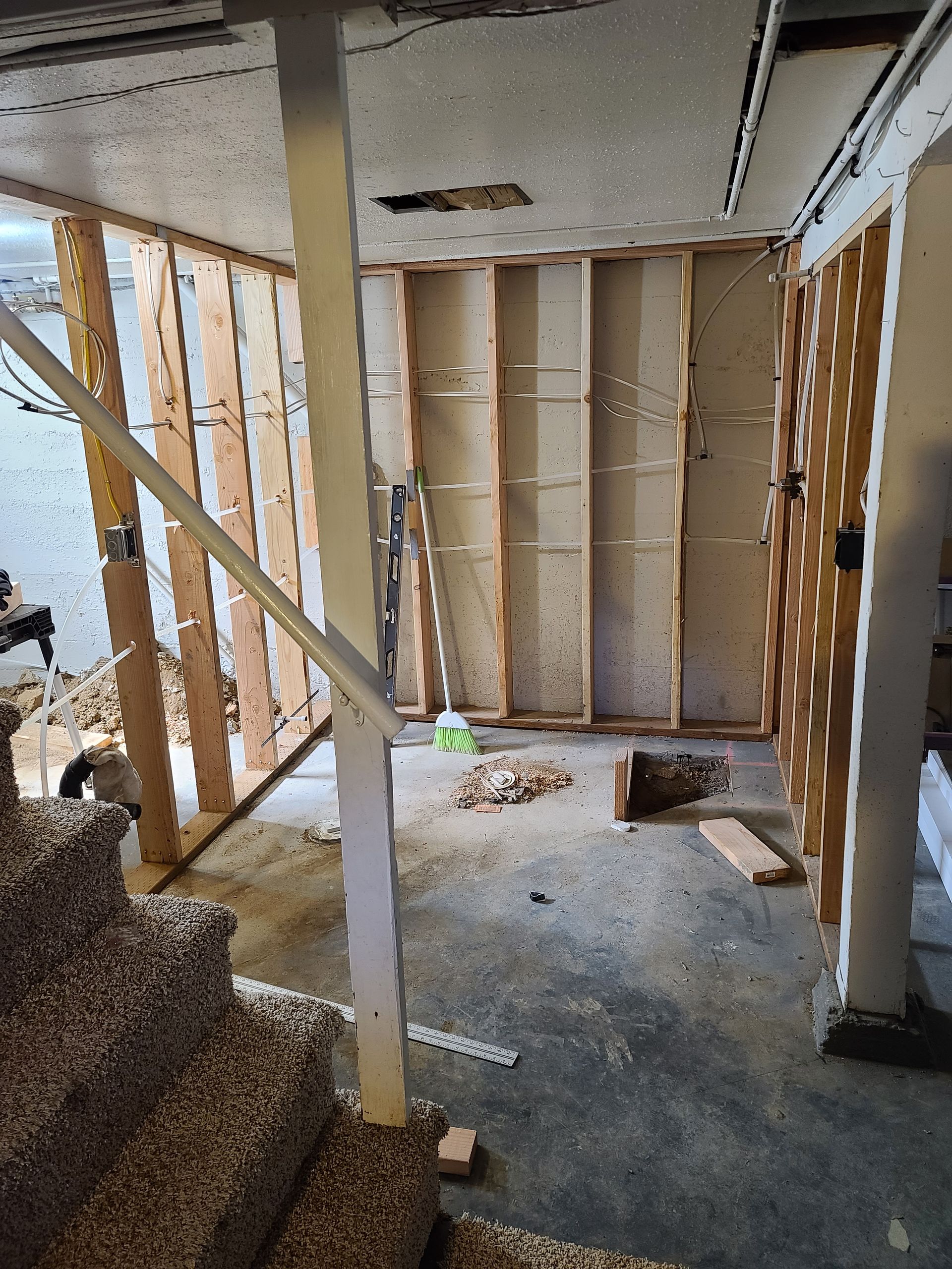 Basement renovation: stairwell, exposed wall studs, concrete floor, white support beam, debris.
