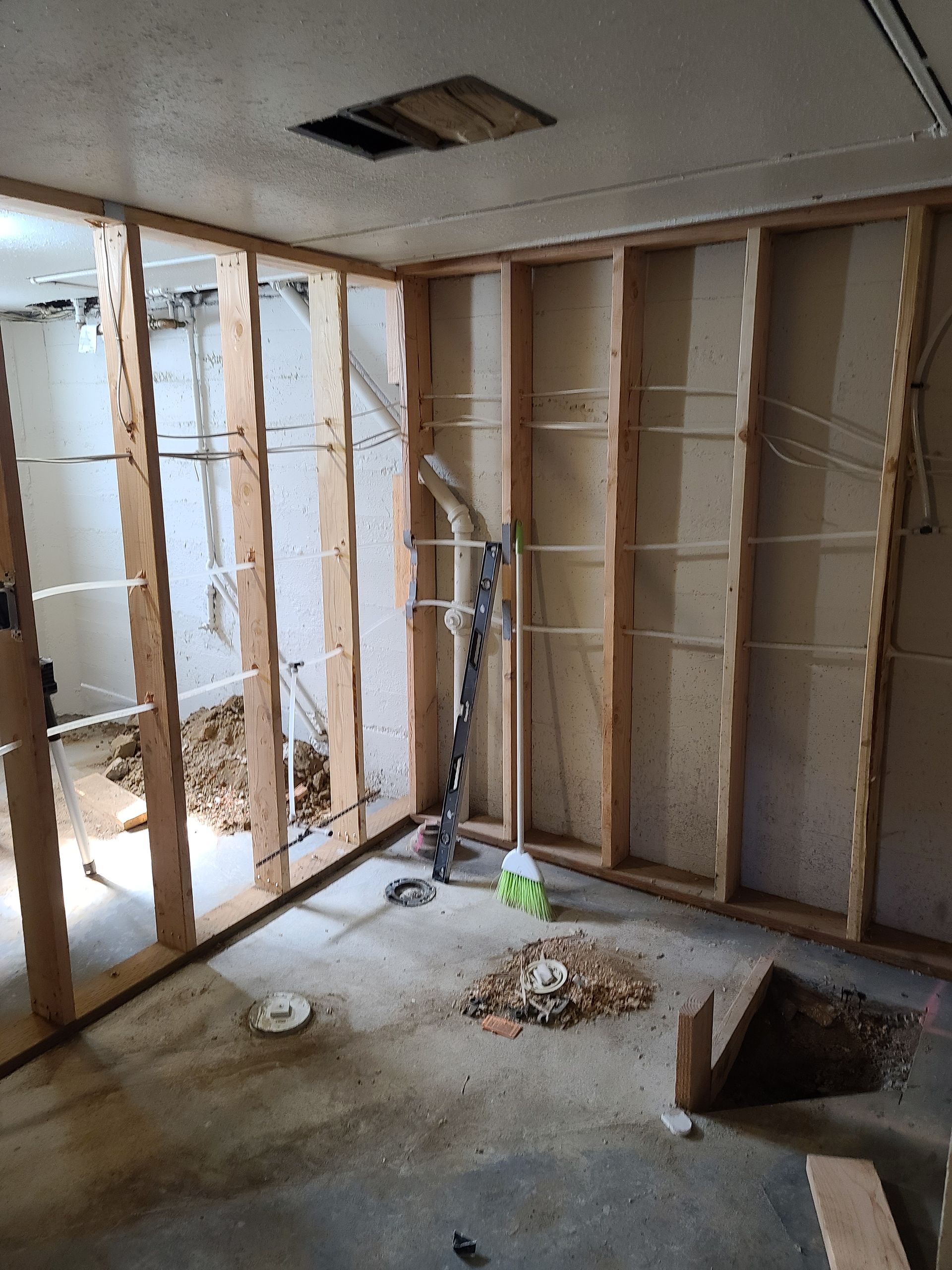 Interior room undergoing construction; exposed wooden wall frames, debris on floor, hole in ceiling.