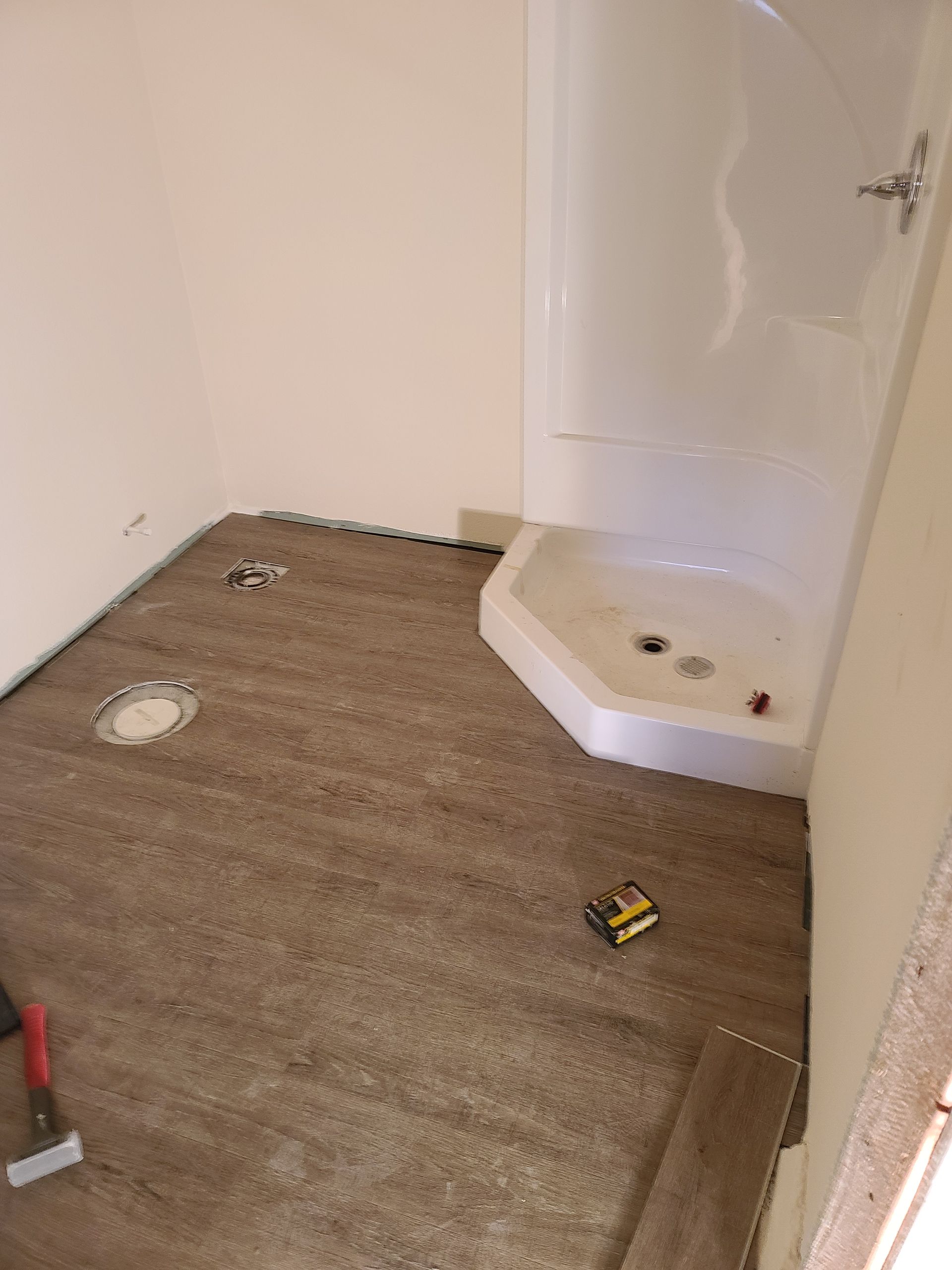 Bathroom renovation with brown flooring, white shower, and walls.