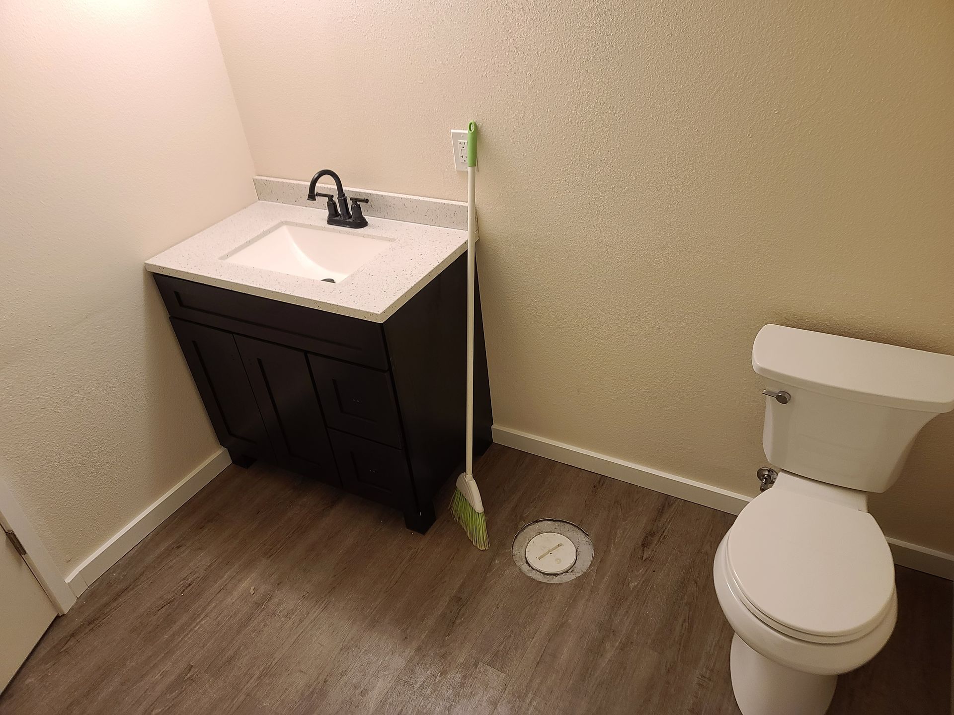 Bathroom with dark vanity, white countertop, toilet, and a mop.