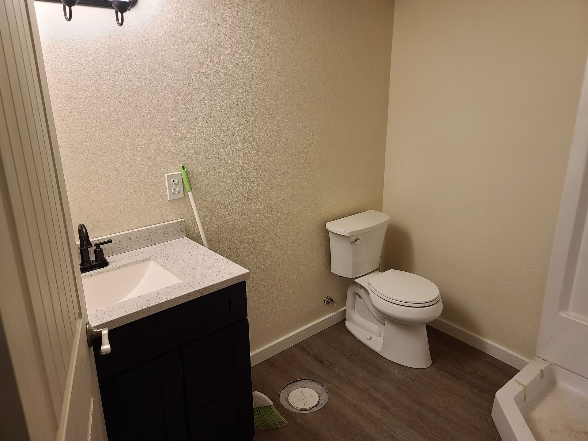 Bathroom with a vanity, toilet, and shower. The walls are neutral colors and floors are wood-like.