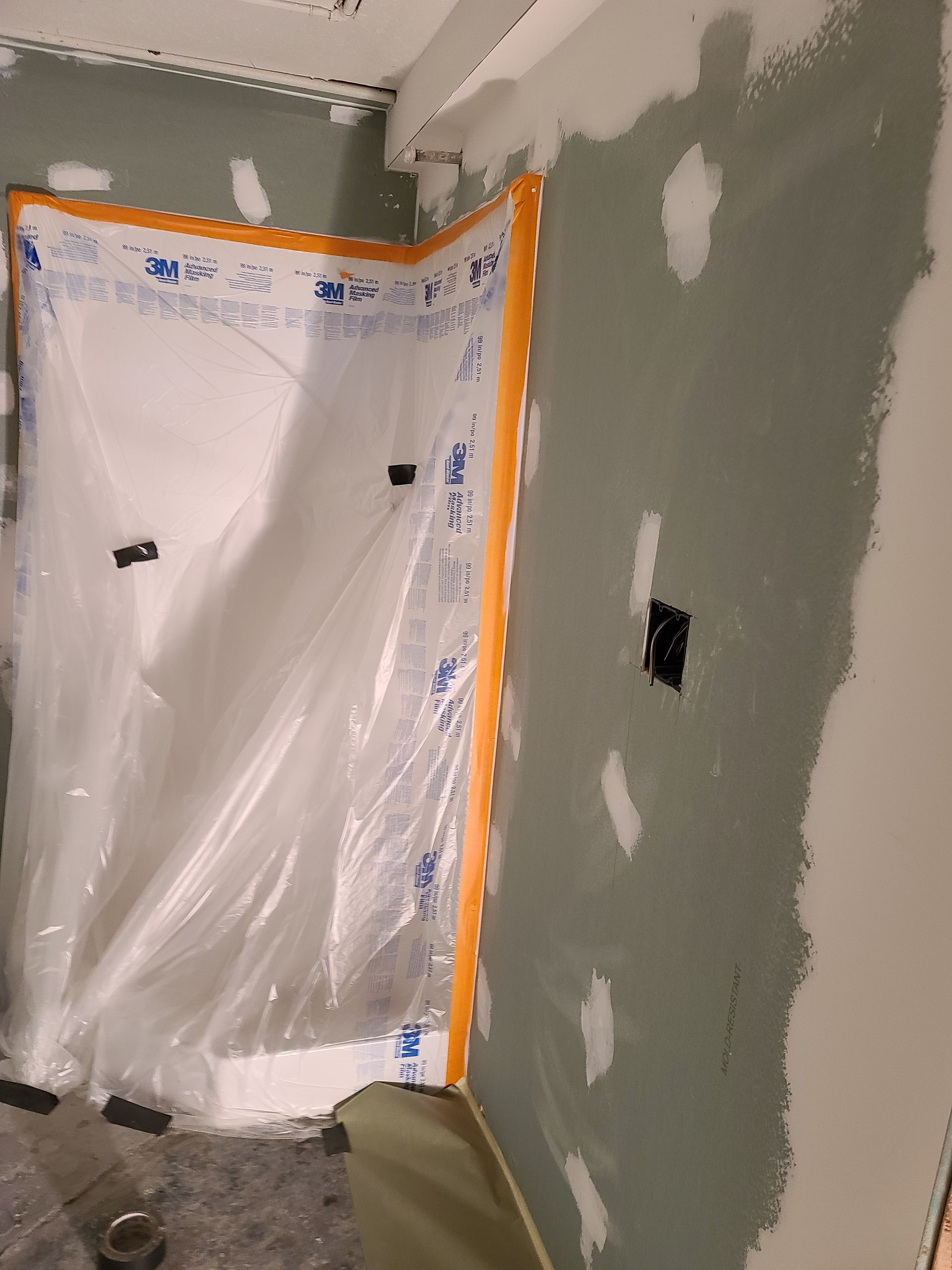 Room under construction, plastic sheeting protects a corner. Green painted drywall with taped seams.