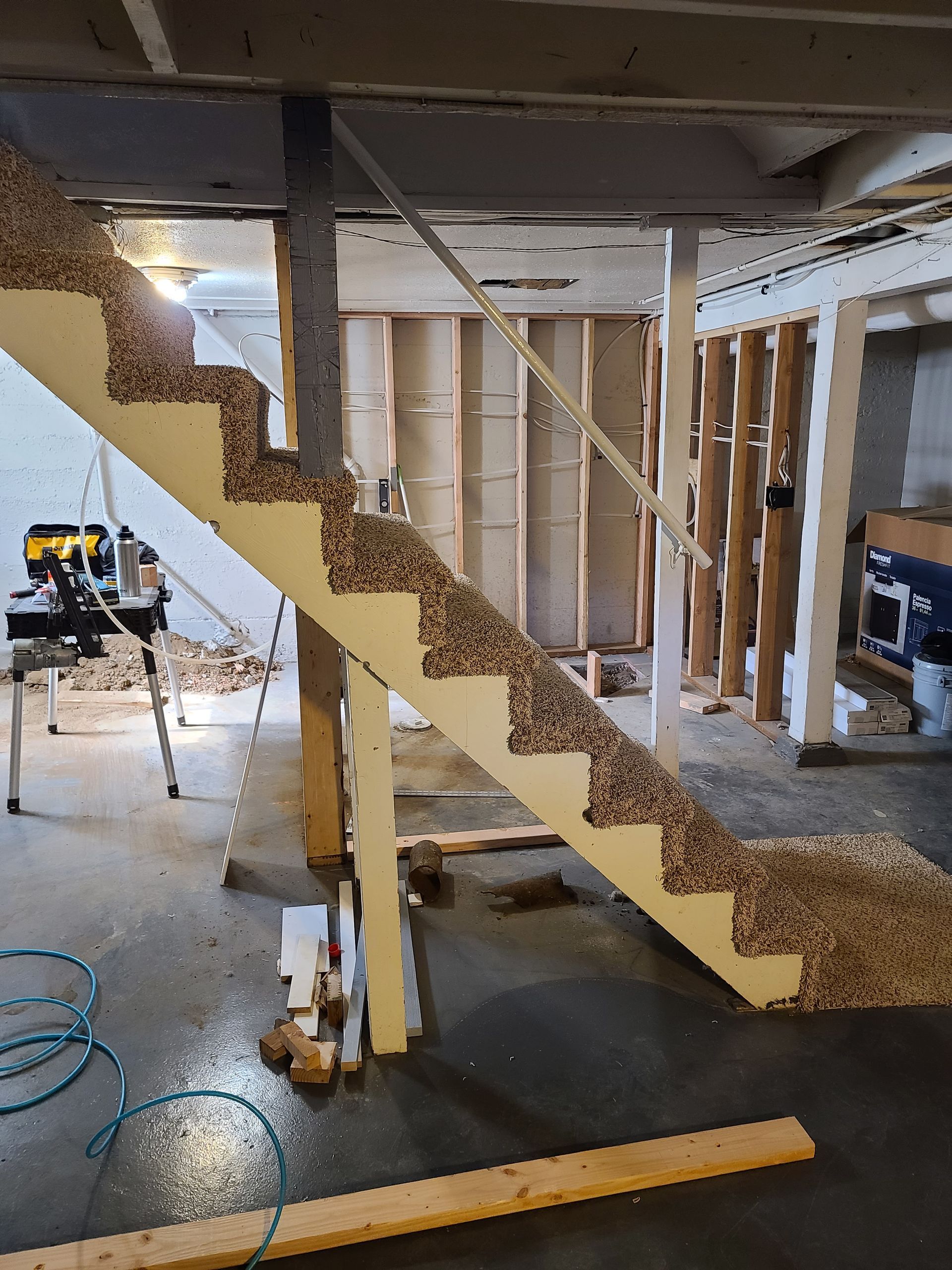 Staircase under construction with carpeted treads. The basement setting includes exposed framing and tools.