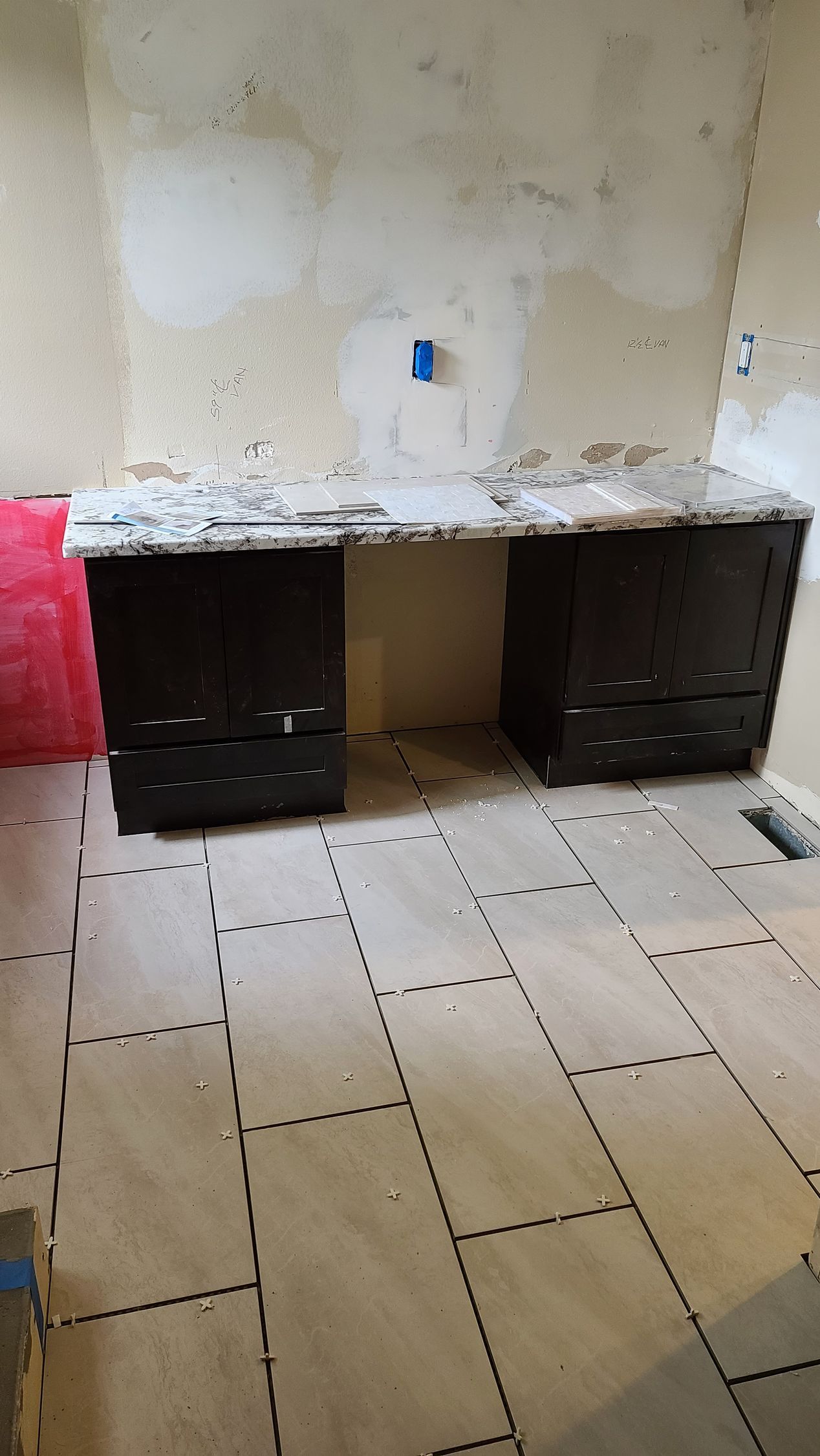 Dark brown desk with drawers, under construction, against a wall with exposed plaster and a tile floor.