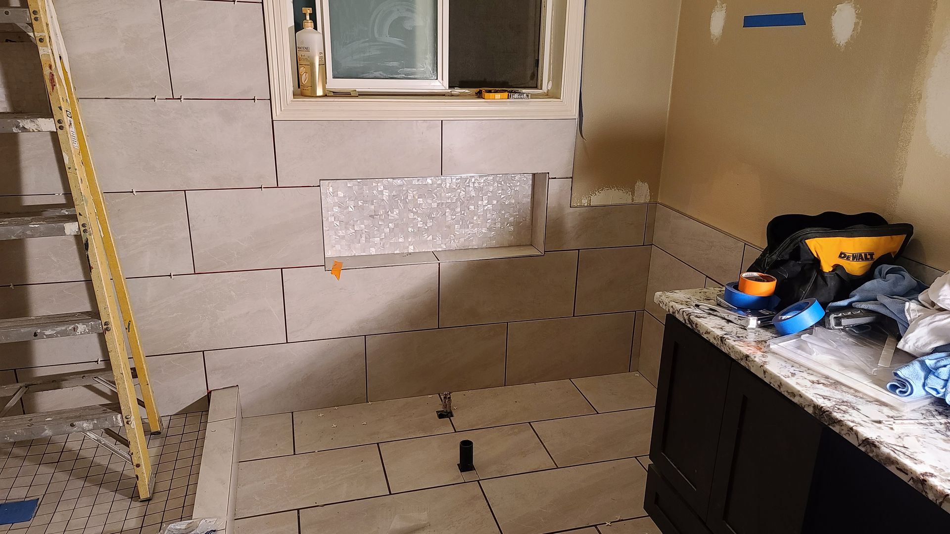 Bathroom renovation in progress. Tiled walls and floor. Window, cabinet, and tools visible.