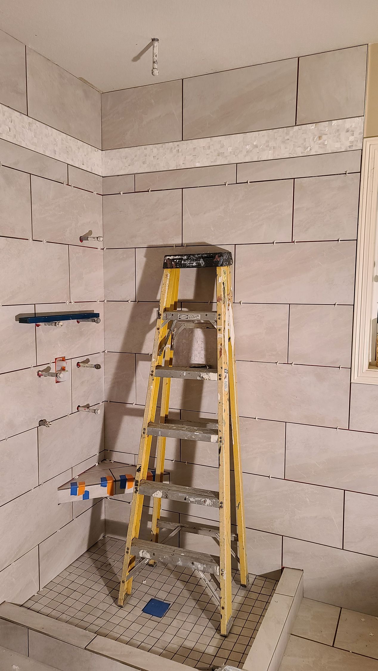 Yellow ladder in tiled shower, plumbing visible. Construction in progress.