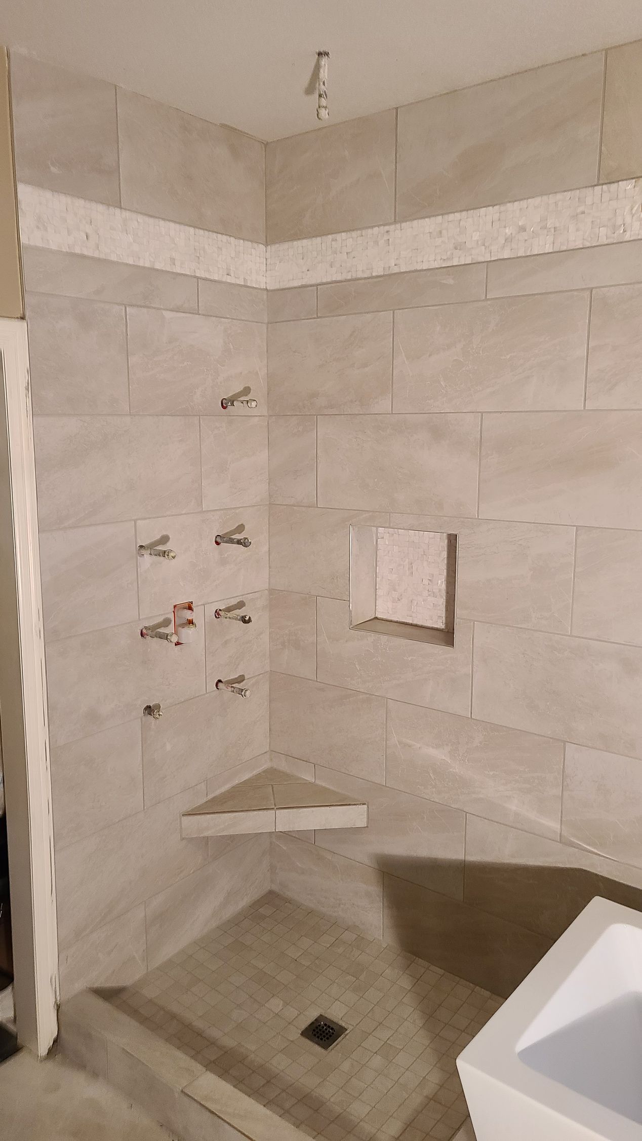Shower stall with beige tiles, corner seat, and multiple showerheads.