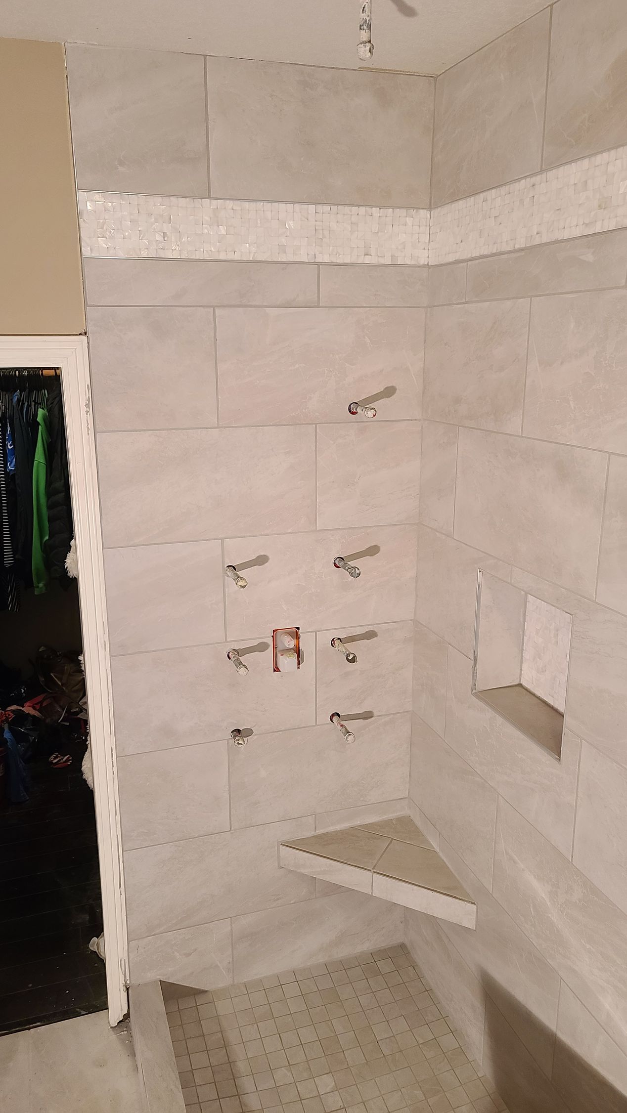 Shower with light gray tile, a decorative mosaic stripe, and plumbing fixtures. A corner seat is installed.
