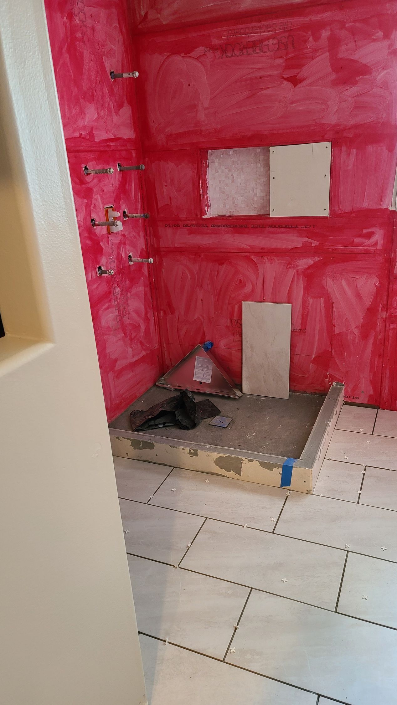 Bathroom under construction; red waterproof membrane covers the shower walls. Floor tile is laid.